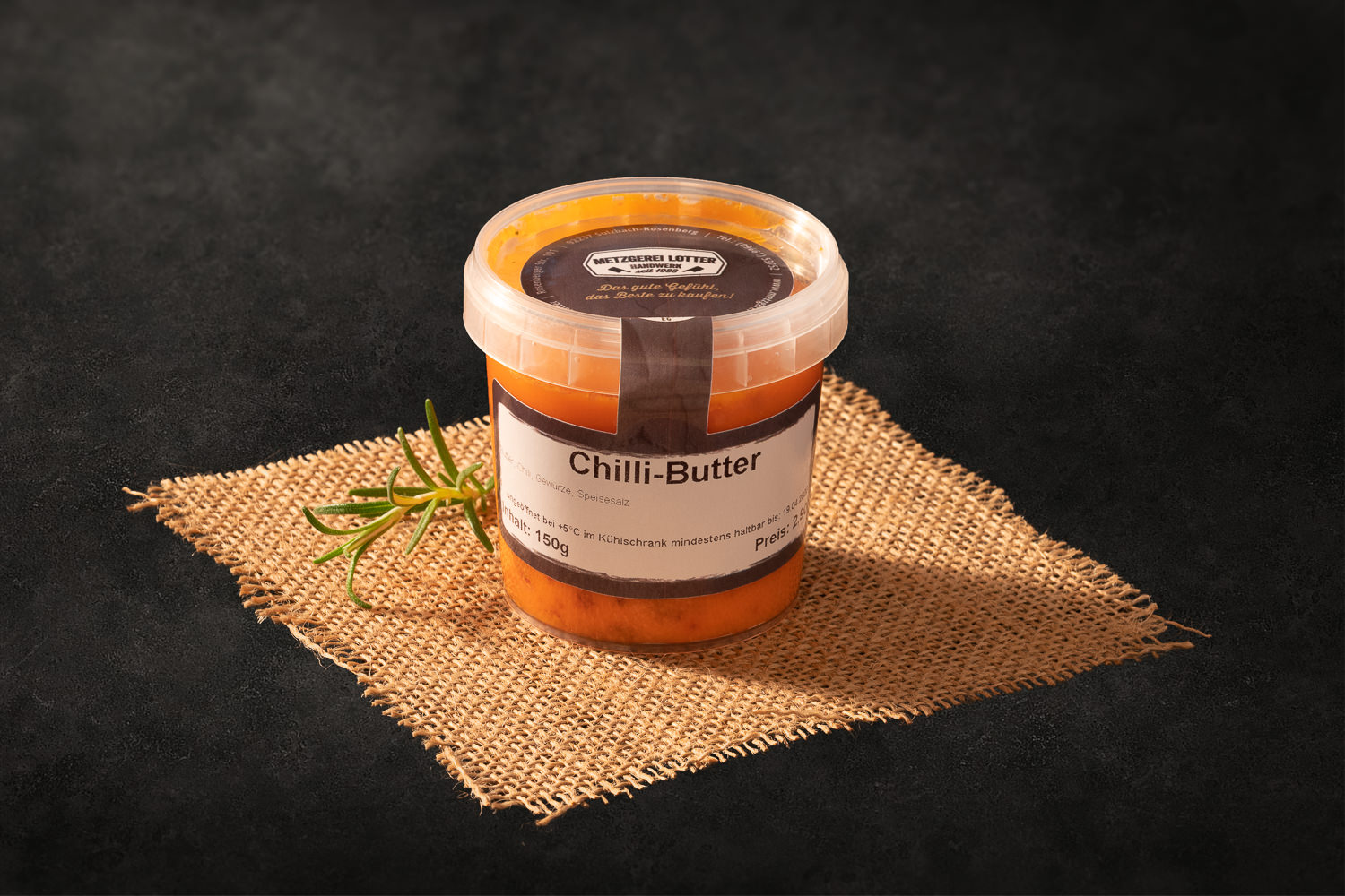 Selbstgemachte Chili-Butter aufgeschnitten auf einem dunklen Holzbrett, dekoriert mit frischer Chili, Pfefferkörnern und Kräutern – würzige Kräuterbutter mit roter Chili, ideal für Grillgerichte und Steaks.