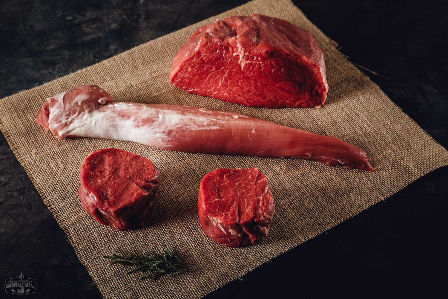 Silvesterpaket Classic von Oberpfalz Beef: Grillfleisch-Auswahl in schwarzer Box mit Steaks, Bratwürsten und Burger-Patties auf dunklem Hintergrund, angerichtet mit Gewürzen, Kräutern und Gemüse – festlich präsentiert für Silvester oder Grill-Events.