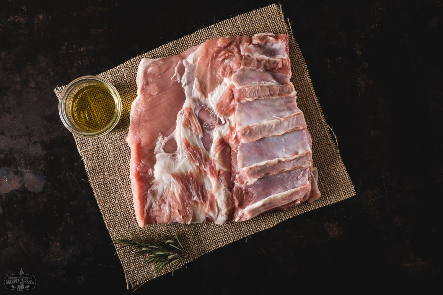 Rohe Kalbsbrust vom Oberpfälzer Milchkalb auf dunklem Untergrund, frisch zugeschnitten mit sichtbarer Marmorierung und Rippenknochen, angerichtet mit Kräutern und Gewürzen – hochwertiges deutsches Kalbfleisch für BBQ oder Schmoren.
