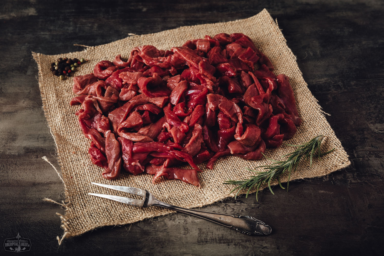 Handgeschnittenes Rindergeschnetzeltes vom Oberpfalz-Rind, roh und frisch, appetitlich auf schwarzem Untergrund angerichtet, begleitet von Rosmarin und Gewürzen – hochwertiges regionales Fleischprodukt.