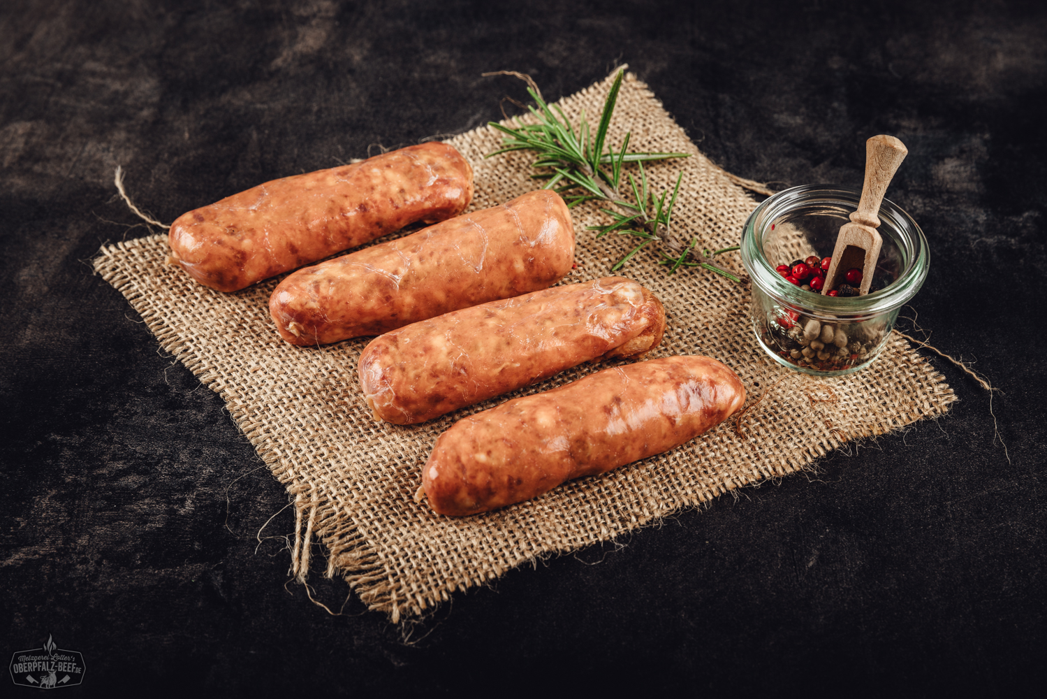 Nahaufnahme von sechs gegrillten Chorizo-Bratwürsten auf einem Grillrost, goldbraun gebräunt mit leichter Röstaroma, im Hintergrund glimmende Holzkohle; rustikales Grillambiente, deutlicher Fokus auf würzige Bratwürste aus regionaler Herstellung.