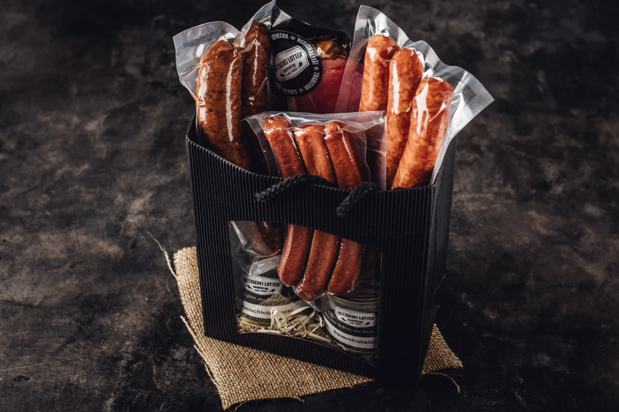Drei hochwertige Oberpfalz-Beef Fleischpakete in eleganter Geschenkverpackung auf rustikalem Holztisch arrangiert, mit frischen Kräutern und dem Oberpfalz-Beef-Logo im Hintergrund – ideal als Premium-Präsent für Fleischliebhaber.