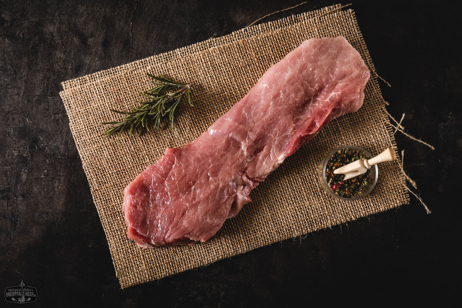 Rohes Schweineschnitzel aus der Oberschale vom Oberpfälzer Landschwein, frisch und saftig auf Holzbrett angerichtet, umgeben von Gewürzen, Kräutern und Knoblauch für die Zubereitung – hochwertiges Fleischprodukt aus der Region Oberpfalz.