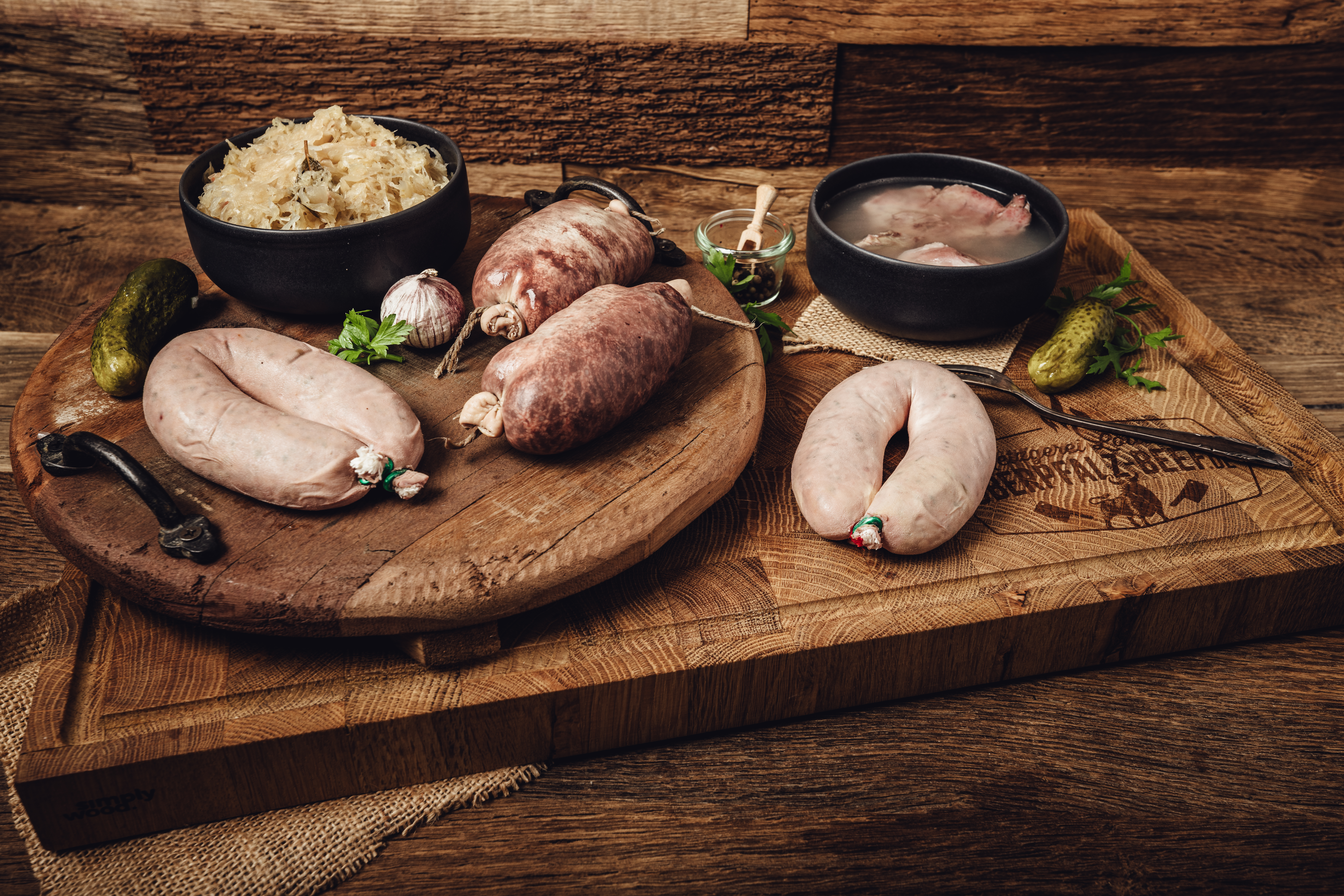 Schlachtschüssel-Platte Maxi – Bayerische Spezialitäten aus der Oberpfalz Gegarte Wildschweinhaxe vom Oberpfälzer Wild auf Holzbrett angerichtet, außen goldbraun und knusprig, umgeben von Rosmarinzweig, frischem Knoblauch und Pfefferkörnern – rustikale Fleischspezialität aus regionaler Jagd.