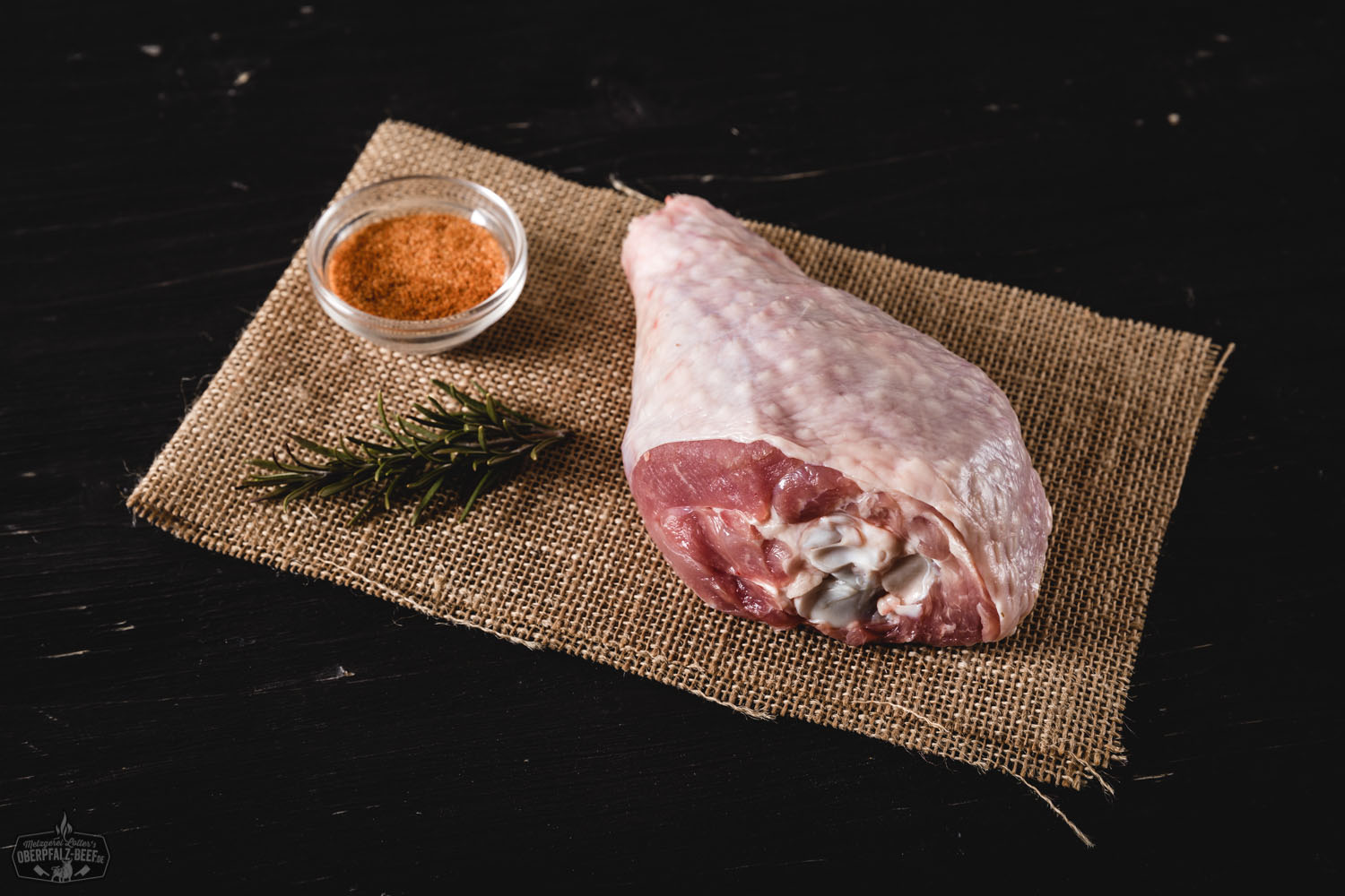 Unterkeulen von der Oberpfälzer Bauernpute – Frisches Geflügelfleisch direkt vom Bauernhof Rohe Unterkeulen von der Oberpfälzer Bauernpute nebeneinander auf Holzbrett angerichtet, umgeben von frischen Kräutern, Knoblauch, Gewürzen und Tomaten – hochwertige regionale Geflügelspezialität für bewusste Ernährung.
