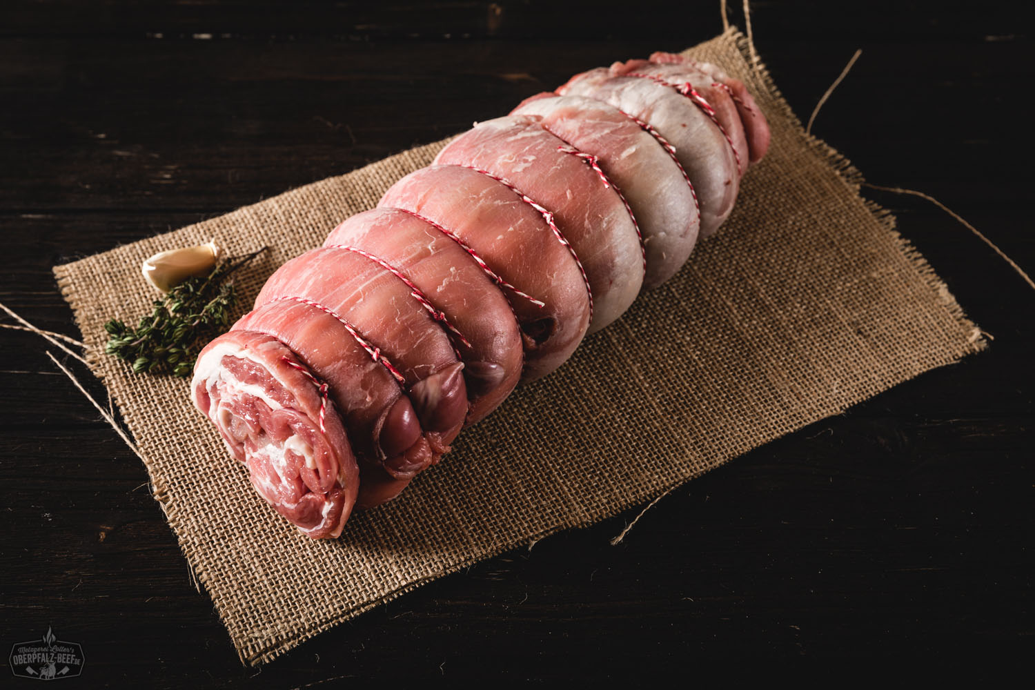 Lammrollbraten aus der Schulter vom Juradistl-Lamm auf Holzbrett angerichtet Lammrollbraten aus der Schulter vom Juradistl Lamm, perfekt gebräunt und saftig, servierfertig auf einem rustikalen Holzbrett mit frischen Kräutern garniert.