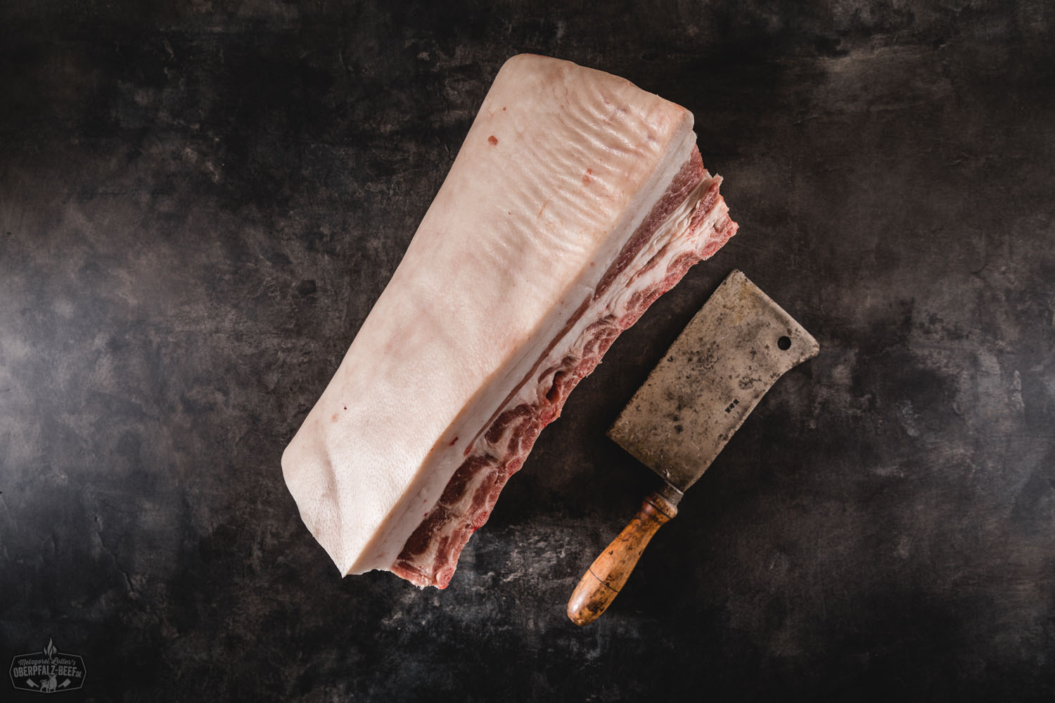 Ganzes Kotelett Classic Cut vom Oberpfälzer Landschwein – trocken gereift für vollen Genuss Rohes Schweinekotelett im Classic-Cut mit Knochen, dick geschnitten und gut marmoriert, auf dunklem Untergrund präsentiert – ideal zum Selberreifen; hochwertiges Fleisch vom Oberpfälzer Landschwein.