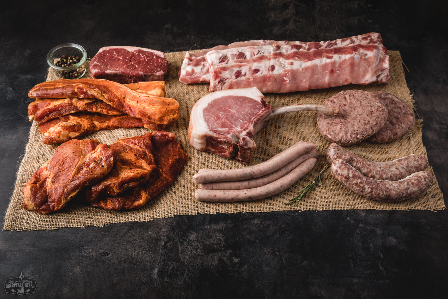 Grillpaket mit hochwertigem Oberpfalz-Beef: Verschiedene Stücke marmoriertes Rindfleisch appetitlich auf Holzuntergrund angerichtet, darunter Tomahawk-Steak, Rumpsteak, Rib-Eye und Würstchen; ideal für Grillfreunde und BBQ-Liebhaber.