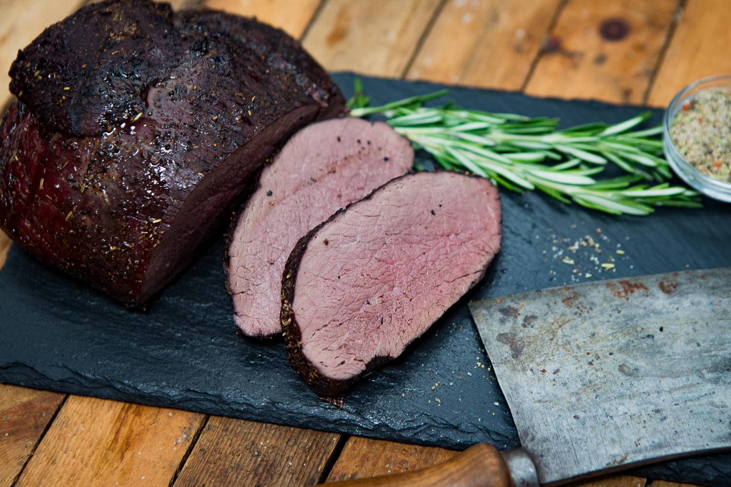 Schulter ohne Knochen vom Oberpfälzer Wildschwein – Regionales Wildfleisch in Premiumqualität Roher Wildschwein-Schulterbraten ohne Knochen aus der Oberpfalz auf dunklem Untergrund, fein marmoriert, angerichtet mit Rosmarin, Knoblauchzehen und bunten Pfefferkörnern – hochwertiges Wildfleisch für nachhaltigen Fleischgenuss.