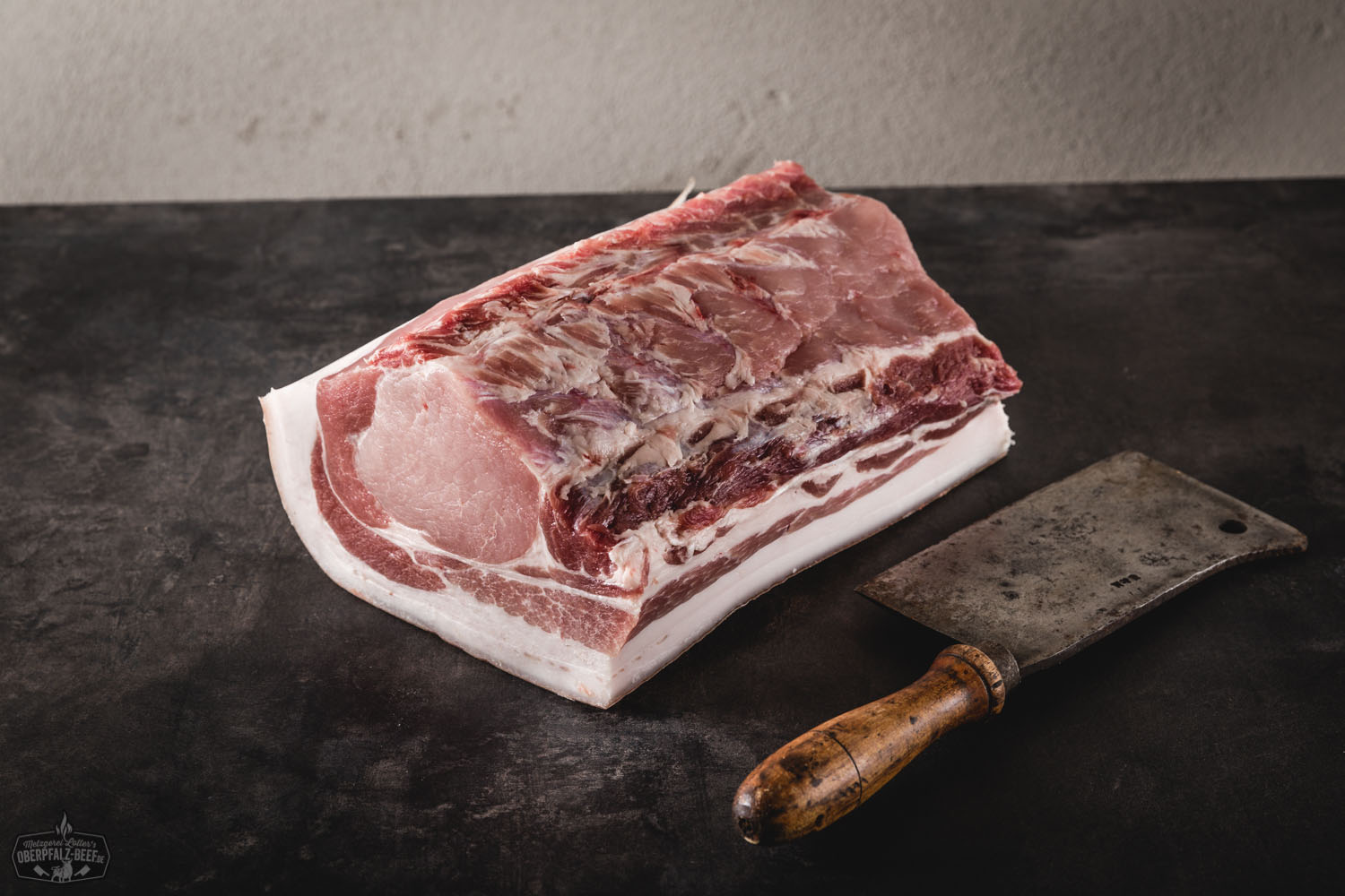 Halbes Dry Aged Kotelett mit Schwarte vom Oberpfälzer Landschwein Halbes Dry-Aged Kotelett vom Oberpfälzer Landschwein mit Knochen und Schwarte auf Holzbrett, stark marmoriert, roh und saftig, appetitlich präsentiert für hochwertige Fleischgenuss-Themen.