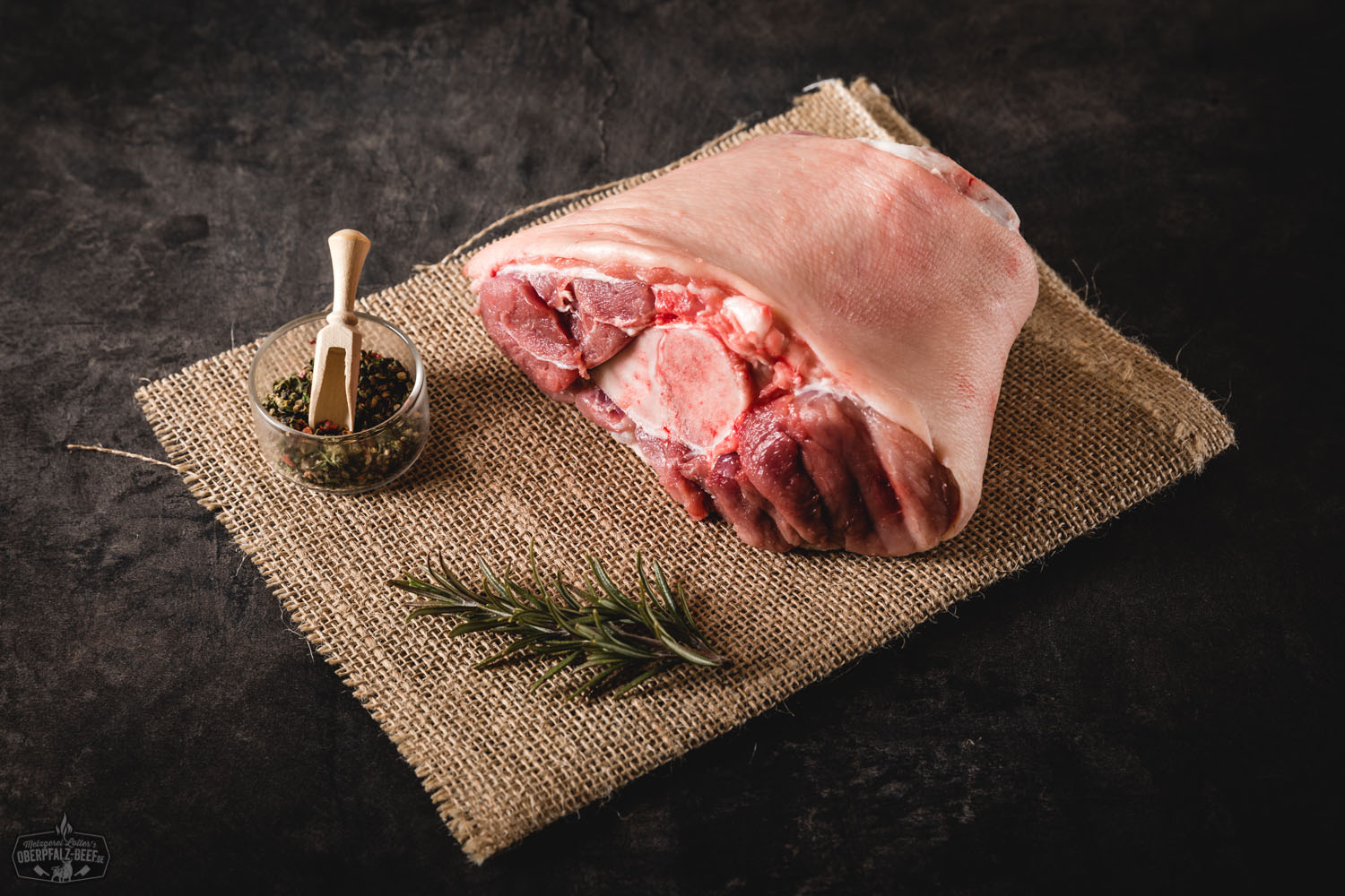 Vordere Haxe vom Oberpfälzer Landschwein – Regionales Schweinefleisch von bester Qualität Rohe vordere Schweinshaxe vom Oberpfälzer Landschwein auf dunklem Untergrund, mit sichtbarer Fettschicht und Muskelstruktur, präsentiert als hochwertiges Fleischstück für traditionelles Schmoren oder Grillen.
