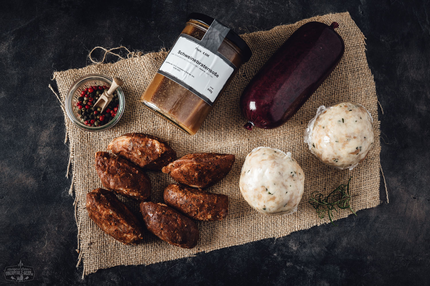 Oberpfälzer Schweinebacken Box mit regionalem Fleisch – online bestellen Mehrere marinierte Schweinebäckchen in vakuumierter Verpackung, angerichtet auf einem dunklen Untergrund mit Kräutern, schwarzem Pfeffer und grobem Salz; hochwertige Fleischspezialität aus der Oberpfalz in Premiumqualität.