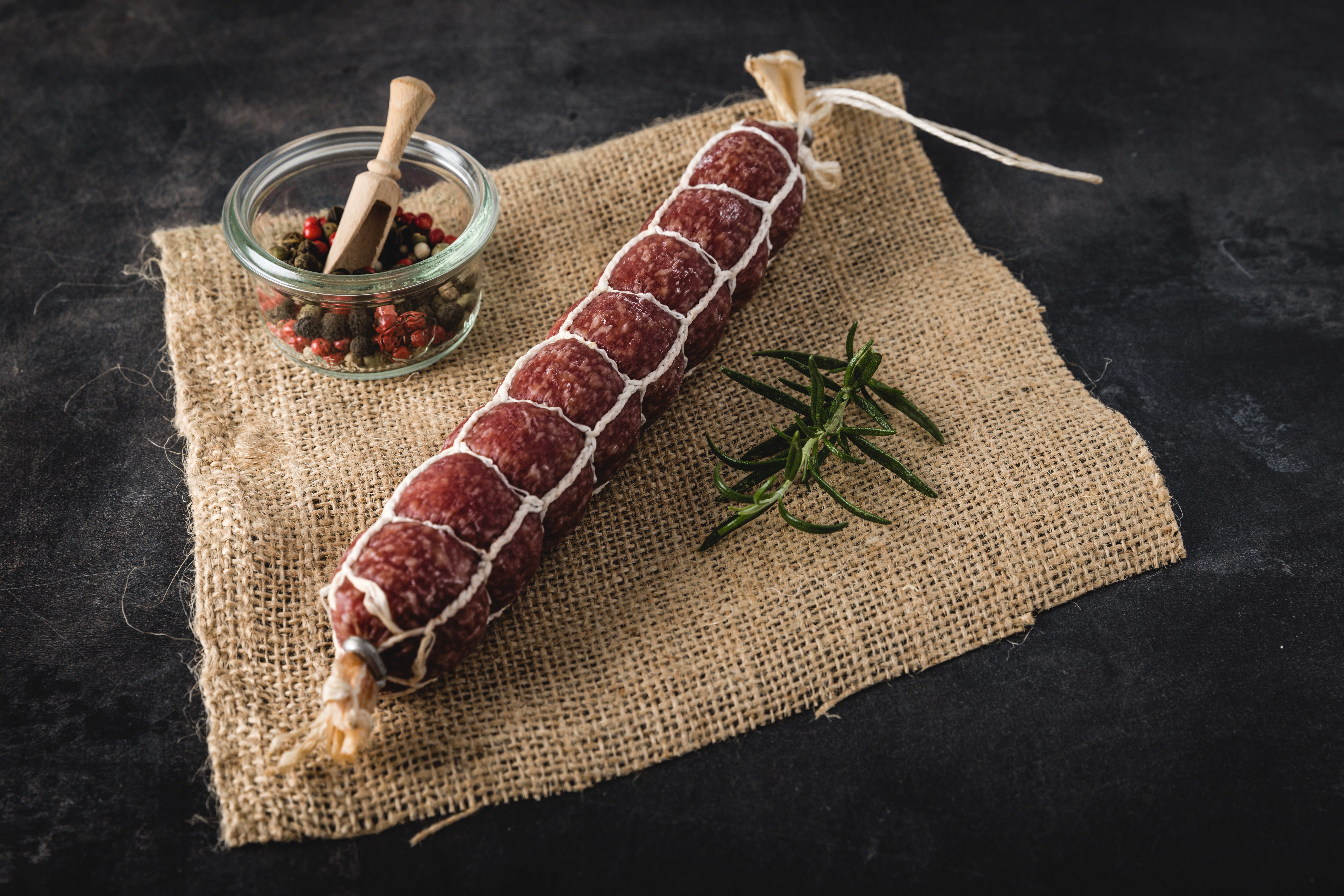 Mandel-Amaretto-Salami – Feine Gourmet-Salami mit Mandeln und Amaretto-Aroma Mandel-Amaretto-Salami auf rustikalem Holzbrett mit Nüssen und Amarettokeksen, ideal für Feinschmecker und Genießer.