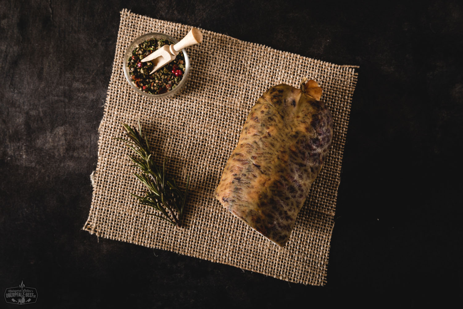 Räucher-Speckwurst aus der Oberpfalz – Hausgemacht & Herzhaft Geräucherte Speckwurst in Nahaufnahme auf einem dunklen Holzbrett, angeschnittene Scheiben zeigen die grobe, würzige Textur mit sichtbaren Speckstücken, daneben ein Messer und rustikale Dekoration – traditionelle bayerische Wurstspezialität.