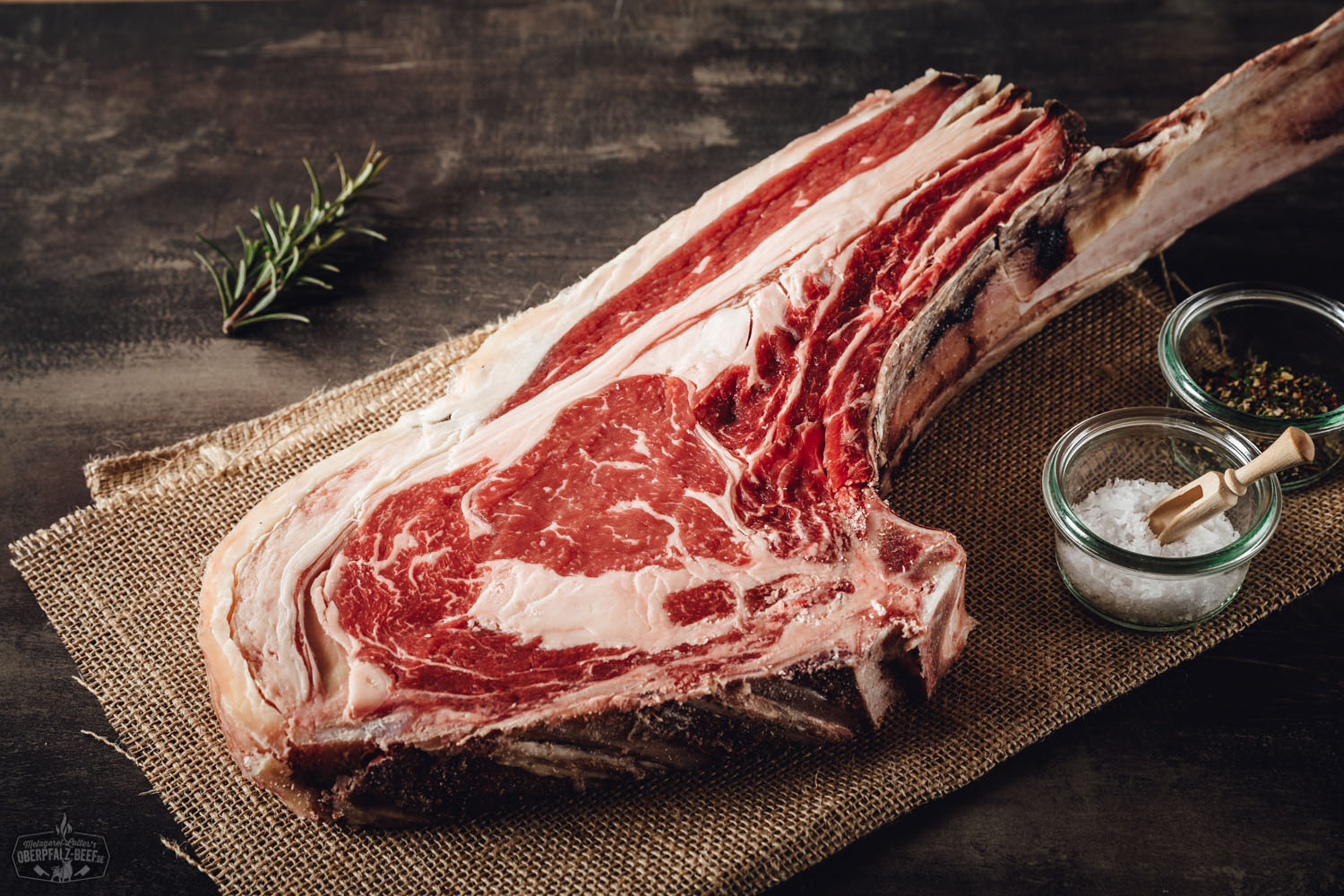 Dry Aged Tomahawk Steak vom Oberpfälzer Rind auf Holzbrett angerichtet Tomahawk-Steak dry aged vom Oberpfalz-Rind auf Holzbrett, saftig gebraten mit sichtbarer Marmorierung, dunkler Kruste und langem Knochen, servierbereit vor rustikalem Hintergrund – hochwertiges Premium-Rindfleisch aus regionaler Zucht.