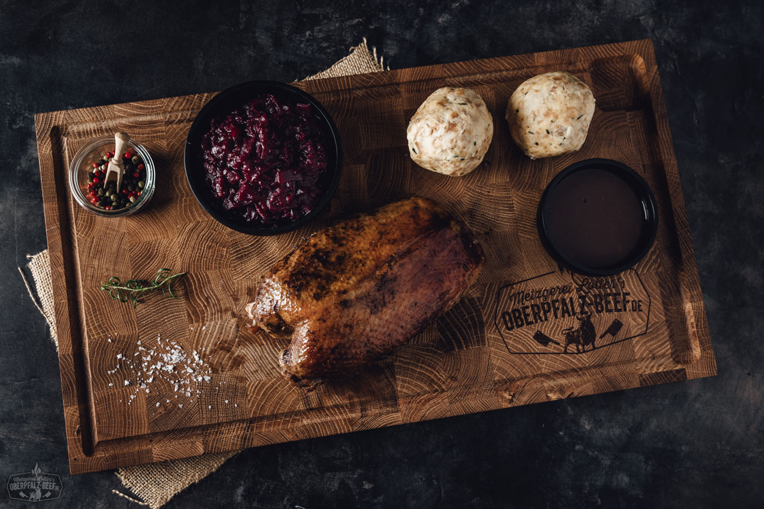 Oberpfälzer Gänsebox mit Gänsebrust – Fertig zubereitetes Festessen online bestellen Goldbraun gebratene Gänsebrust mit knuspriger Haut auf rustikalem Holzbrett, serviert mit dunkelbrauner Bratensauce, dazu Preiselbeeren und frischer Rosmarin – traditionelle Oberpfälzer Gänsebox, appetitlich angerichtet für das Weihnachtsessen.