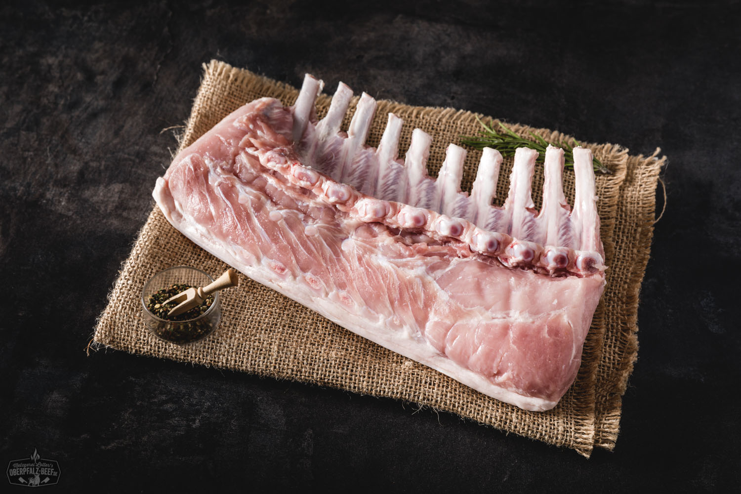 Spanferkelracks vom Oberpfälzer Landschwein auf Holzplatte angerichtet Spanferkelracks vom Oberpfälzer Landschwein, knusprig gebraten mit goldbrauner Kruste, serviert auf rustikalem Holzbrett und garniert mit frischen Kräutern – perfektes Grillgericht aus regionaler Zucht.