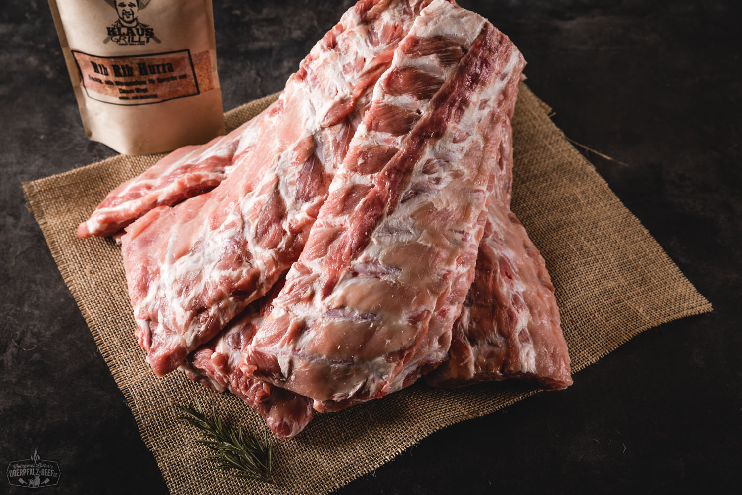 Grillfertiges Baby Back Rib Paket mit mehreren marinierten Schweinerippchen auf schwarzem Untergrund, vakuumverpackt und etikettiert – hochwertiges Fleischprodukt für BBQ und Smoker.