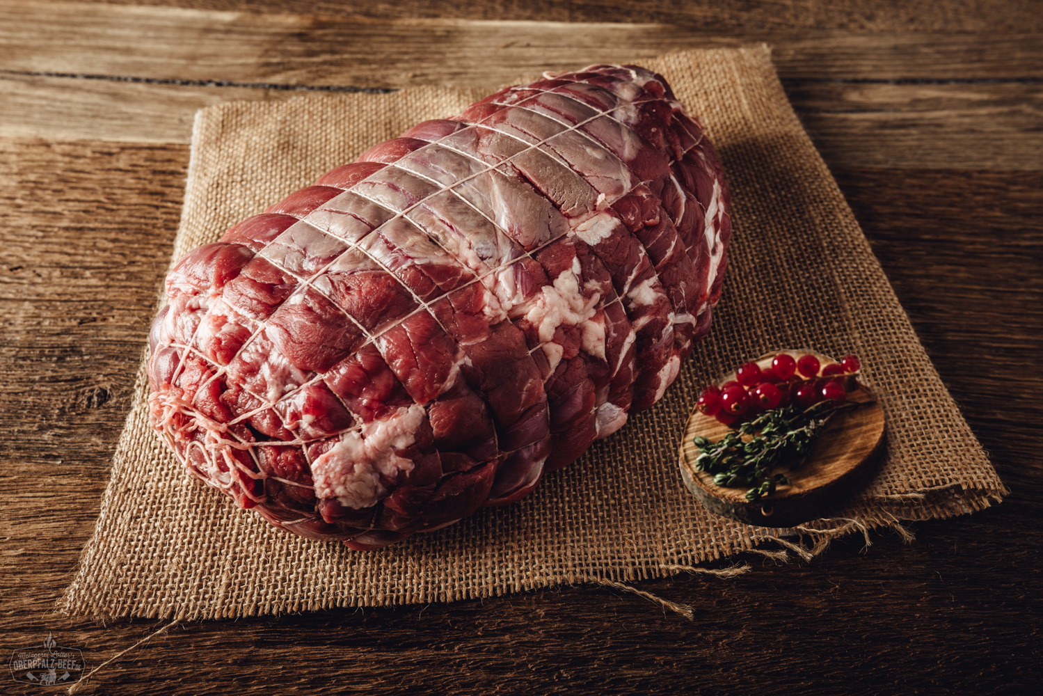 Rollbraten vom Oberpfälzer Hirsch, angerichtet auf einem Holzbrett mit Rosmarinzweig, Knoblauchzehe und grobem Pfeffer – perfekt gegartes, saftiges Wildfleisch mit gut sichtbarer Füllung, appetitlich aufgeschnitten und rustikal präsentiert.