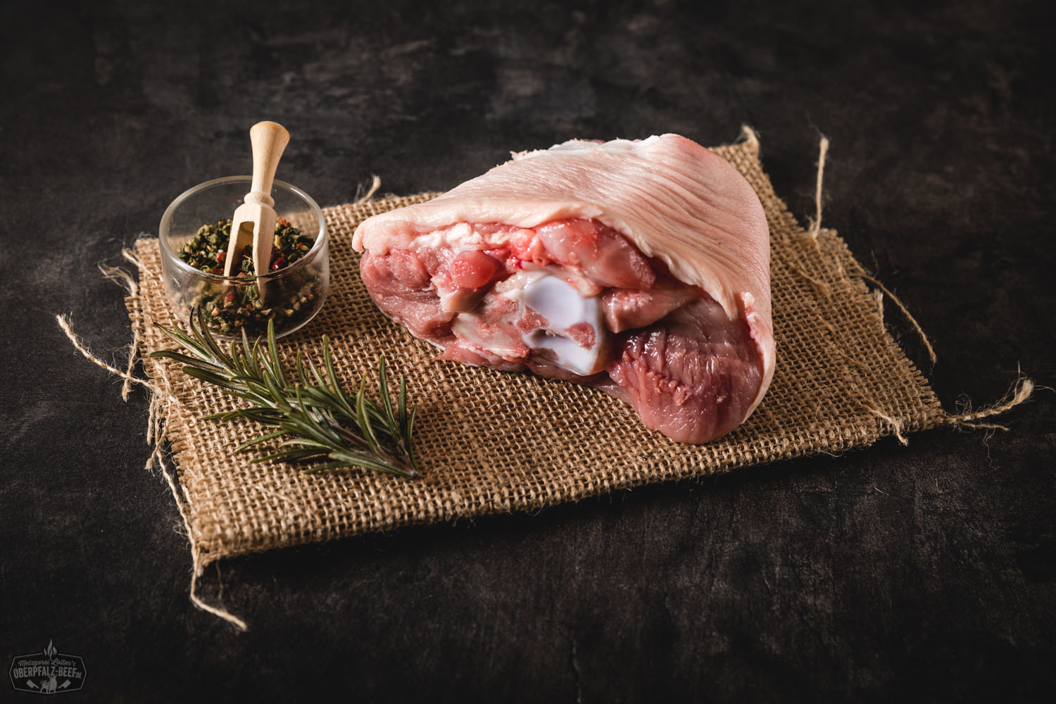 Gegarter Spanferkel-Vorderhaxe vom Oberpfälzer Landschwein auf Holzbrett, knusprige Kruste, saftiges Fleisch sichtbar, serviert mit Petersilie, rustikales Setting – hochwertige Spezialität aus regionaler Herstellung.