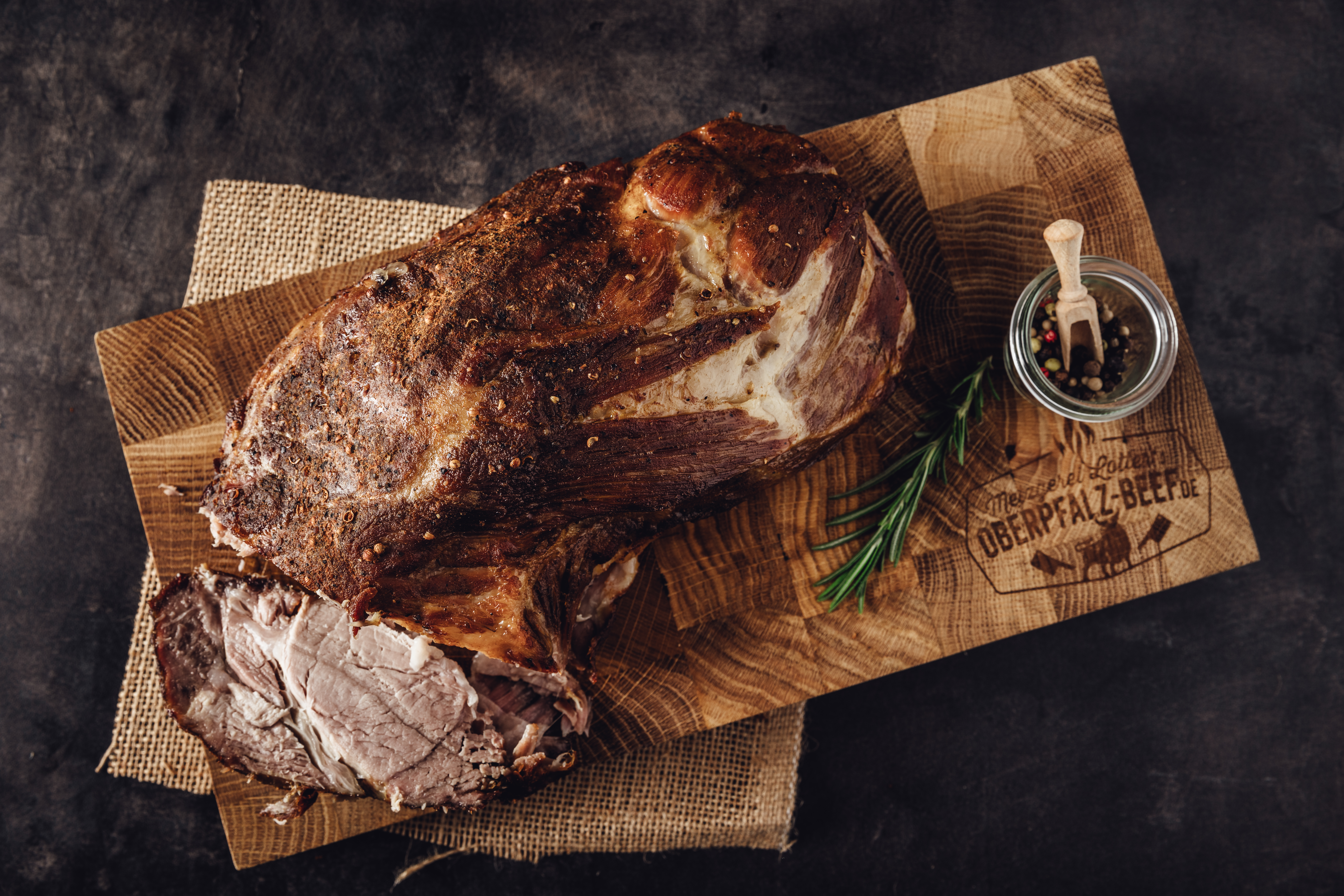 Schweinebraten aus dem Hals - Rezept und Zubereitungstipps Bild eines saftigen Schweinebratens aus dem Hals, perfekt gebräunt und appetitlich auf einem Holzbrett angerichtet, umgeben von frischen Kräutern, ideal für traditionelle bayerische Küche und Fleischliebhaber.
