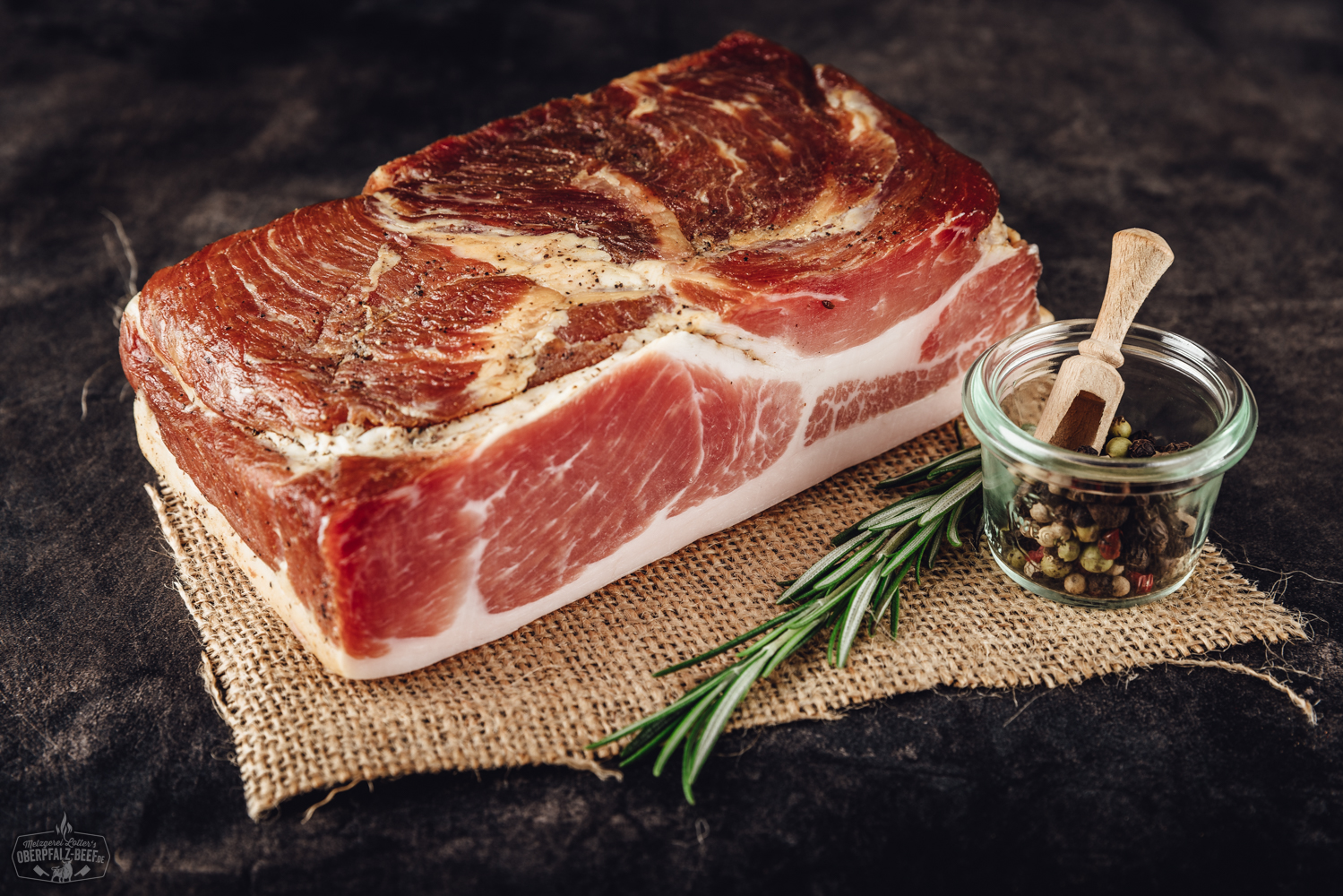 Geschnittene Scheiben von luftgetrocknetem Schinken der Marke Lotter’s, appetitlich auf einem hellen Holzbrett angerichtet, mit Kräutergarnitur und rustikalem Hintergrund – hochwertige, regionale Spezialität aus der Oberpfalz.