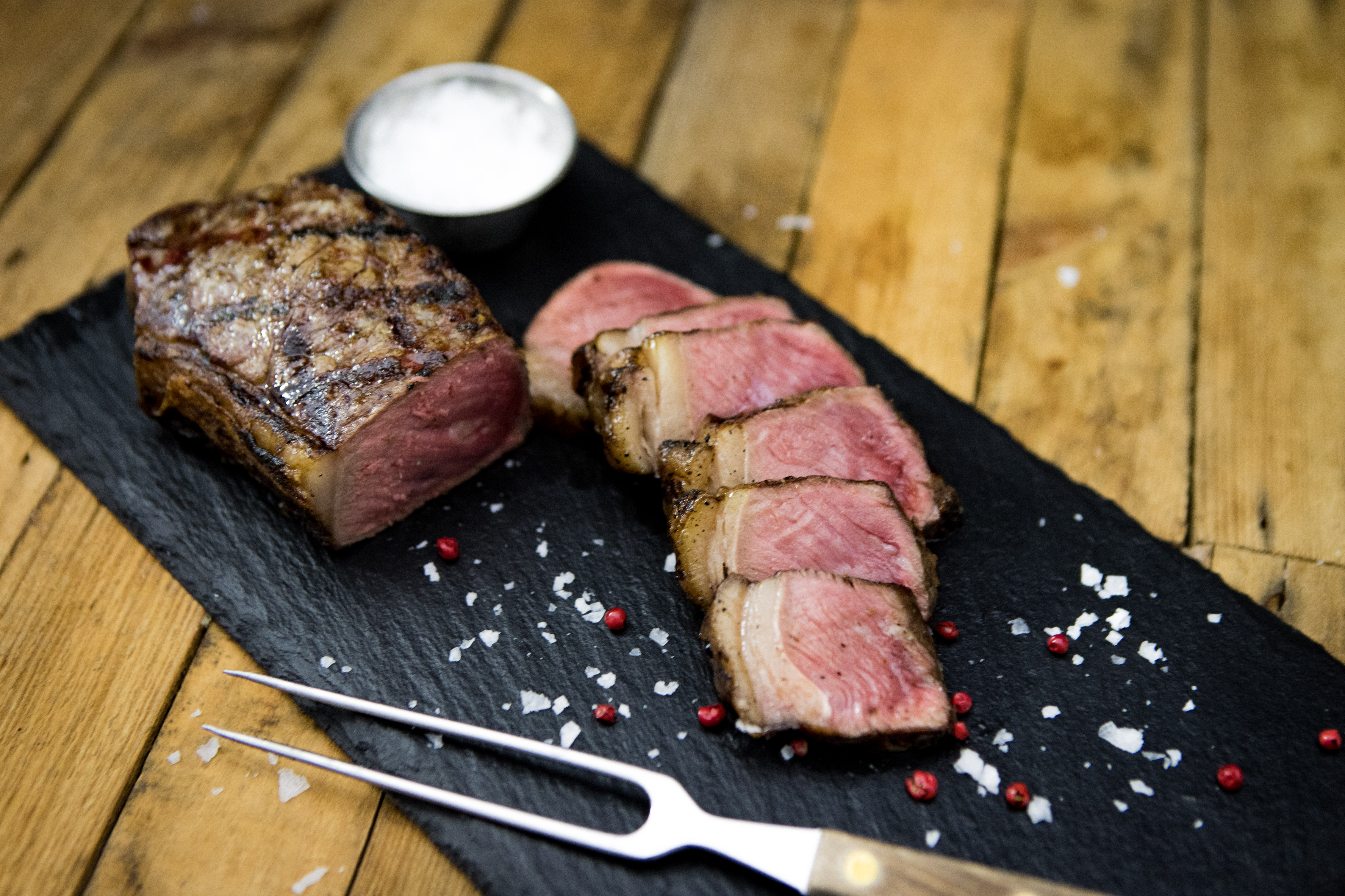 Roastbeef am Stück – Wet Aged vom Oberpfalz-Rind in Premium-Qualität Roastbeef Steak vom Rind, medium gebraten, aufgeschnitten und saftig rosa im Inneren, auf einem dunklen Holzbrett angerichtet, daneben grobes Meersalz, Pfeffer und frische Rosmarinzweige – hochwertiges Rindfleisch in rustikaler Präsentation.