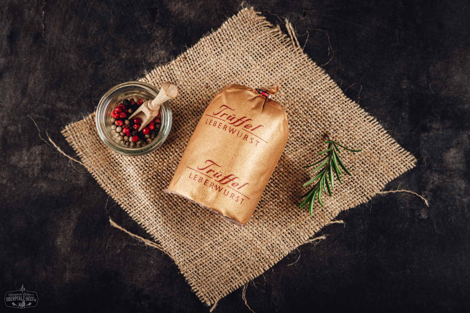 Trüffel-Kalbfleisch-Leberwurst im Glas – Feinkost aus der Oberpfalz Nikolaus-Salami in Portionsgröße mit roter Weihnachtsverpackung, weißem Nikolaus-Motiv und goldener Aufschrift „Nikolaus Salami“; dekorativ arrangiert auf Holztisch mit Tannenzweigen – festliche Wurst-Spezialität aus der Oberpfalz.
