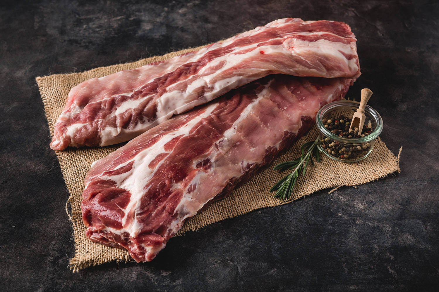 Frisch gegrillte Babyback Ribs mit knuspriger Kruste und intensiver Fleischstruktur auf Holzbrett angerichtet, glasiert mit Barbecue-Soße, daneben Gewürze und frische Kräuter – saftige Spareribs perfekt zum Grillen oder BBQ-Abend.