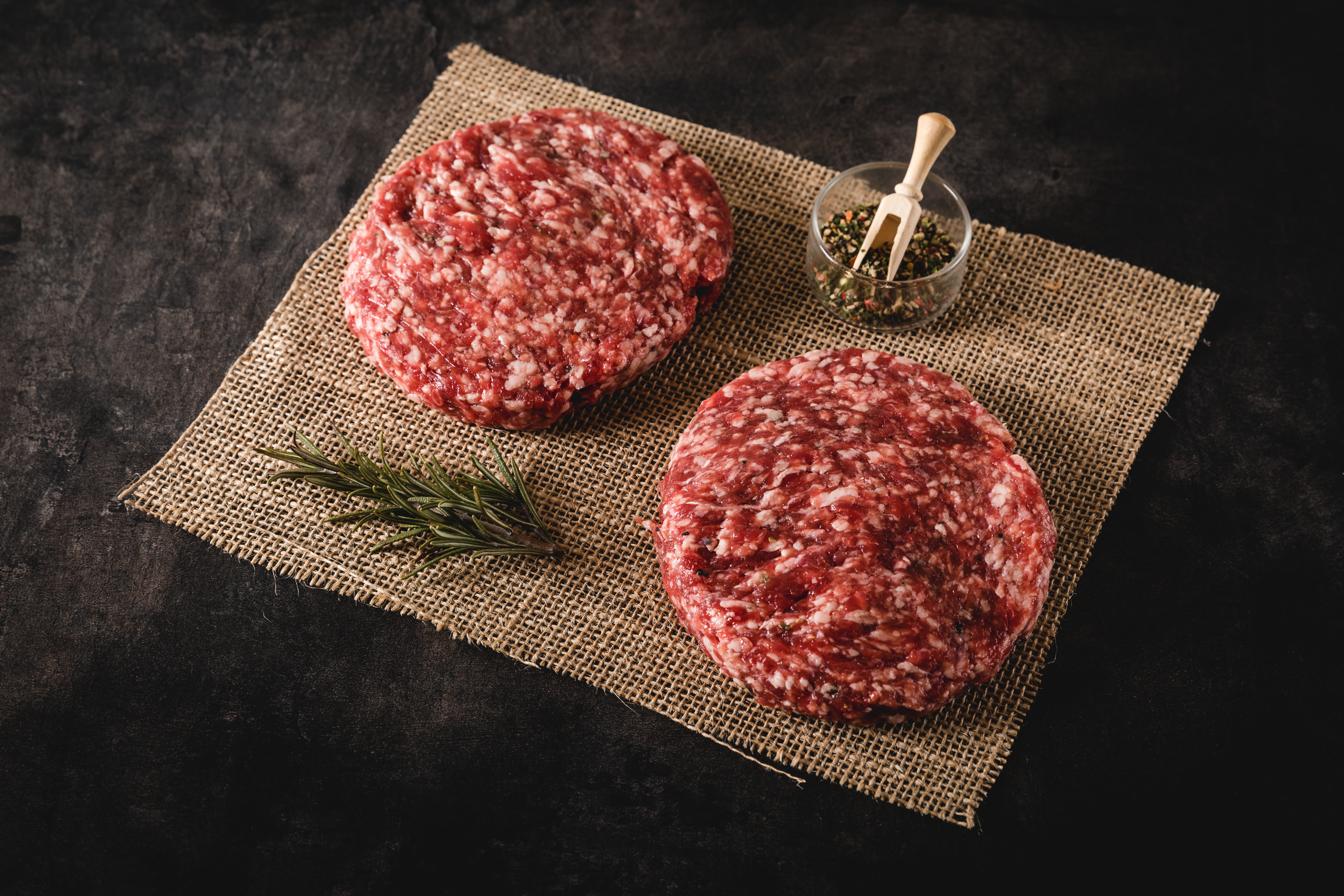 Wet Aged Patties aus Oberpfalz Beef - Hochwertiges Rindfleisch für saftige Burger Wet-aged Beef Patties auf einem Schneidebrett mit Gewürzen und Kräutern – Premium Oberpfalz-Rindfleisch, perfekt für saftige Burger.