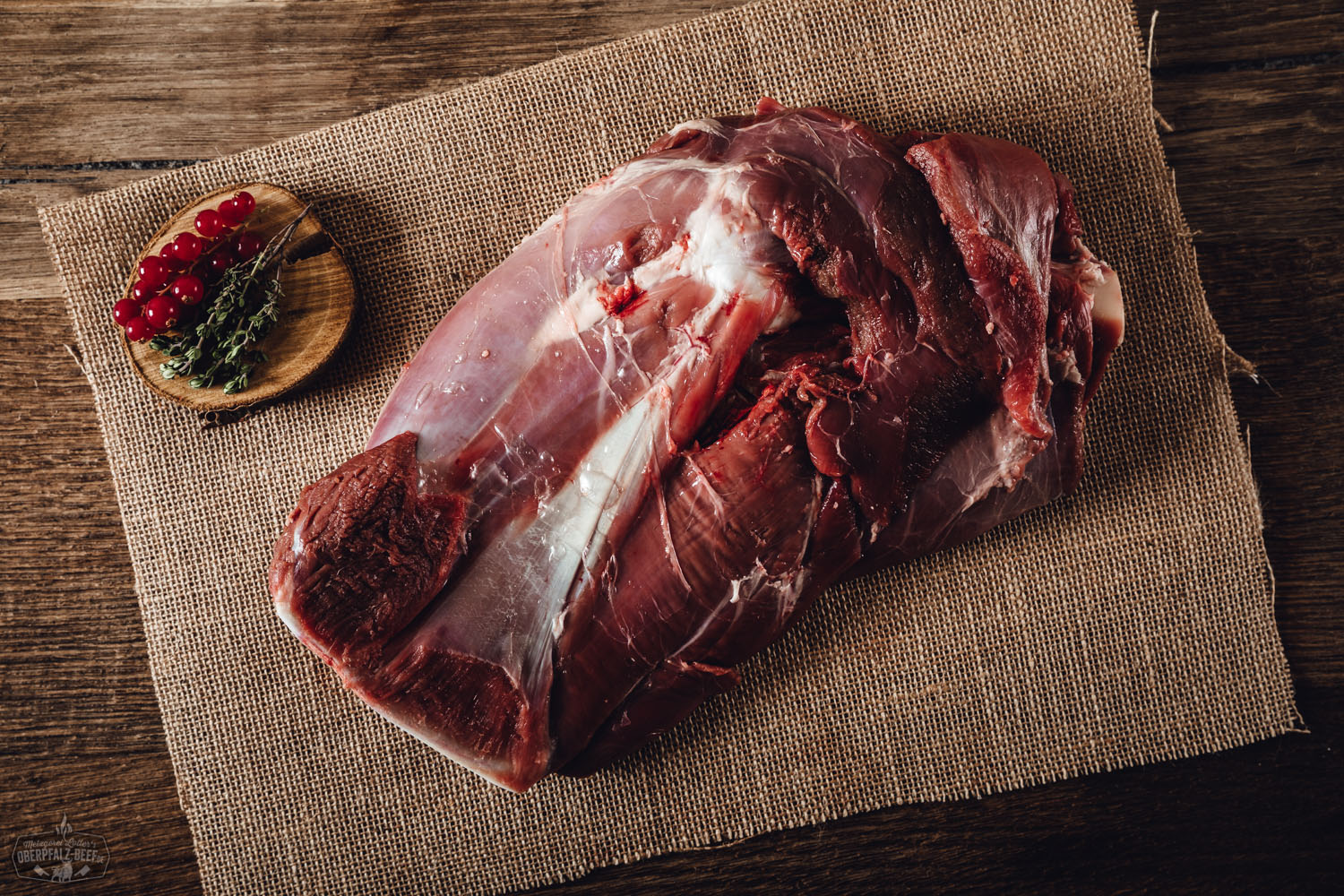 Hirschschulter mit Knochen vom Oberpfälzer Wild – Frisches Wildbret aus regionaler Jagd Schulter mit Knochen vom Oberpfälzer Hirsch auf einem Holzbrett präsentiert, umgeben von frischen Kräutern und Gewürzen, ideal für Wildfleisch-Liebhaber und kulinarische Genießer.
