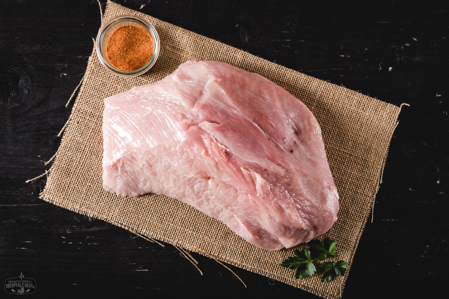 Rohes Brustfilet von einer Oberpfälzer Bauernpute auf dunklem Untergrund, von frischen Kräutern, Gewürzen und Gemüse wie Knoblauch und Tomaten umgeben – hochwertiges Geflügelfleisch aus regionaler Aufzucht.