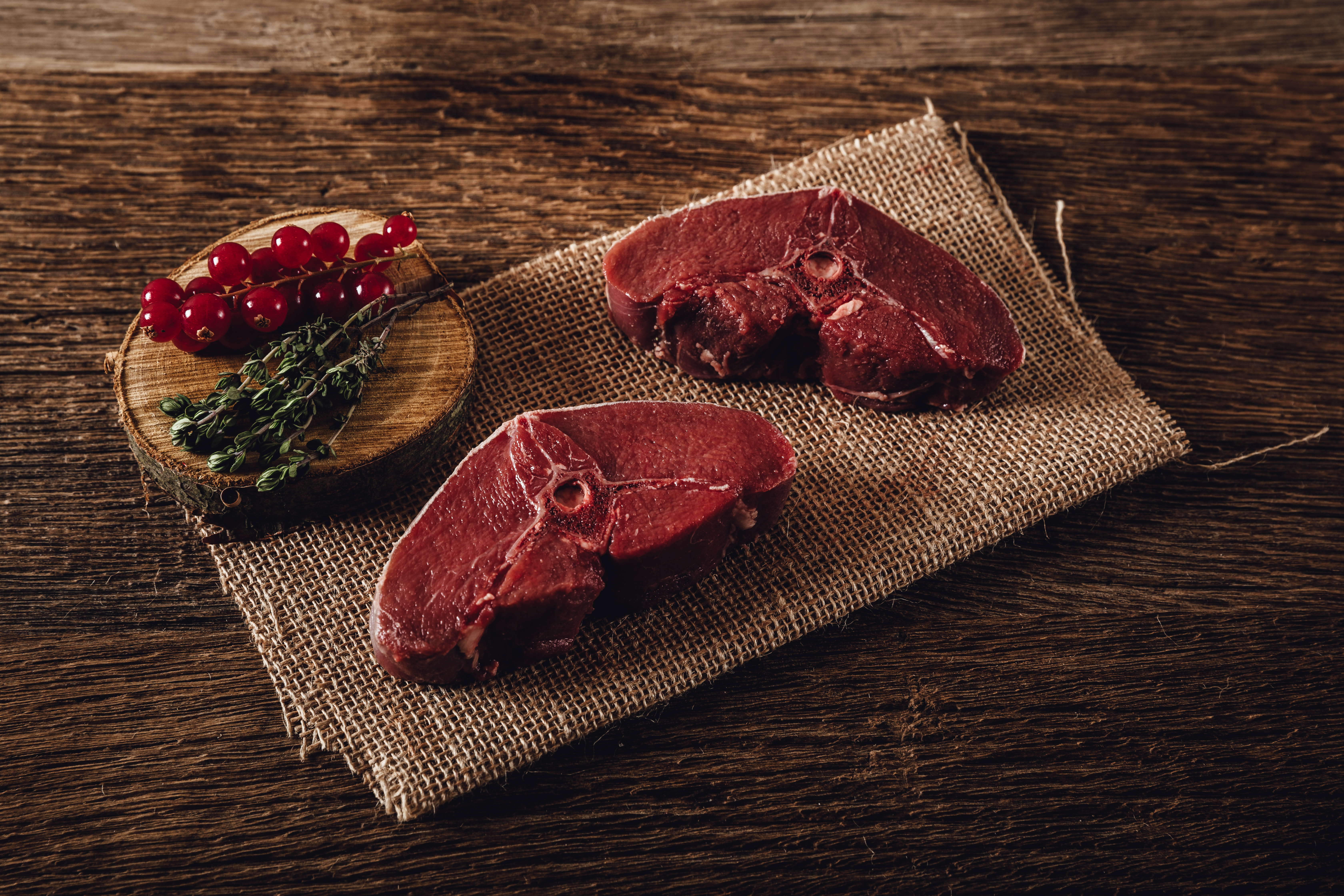 Wildfleisch aus der Oberpfalz - Hochwertiges regionales Fleisch 2018 Ein rohes Wildschweinsteak auf einem rustikalen Holzbrett, dekoriert mit frischen Kräutern und einem Messer. Perfekt für ein besonderes Wildgericht.