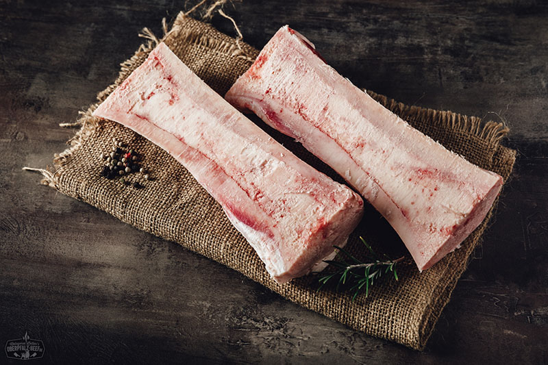 Rinder-Markknochen vom Oberpfalz-Rind roh auf dunklem Untergrund präsentiert, längs aufgeschnitten mit gut sichtbarem Knochenmark in der Mitte – hochwertiges regionales Rindfleisch-Produkt für Brühen und Gourmetgerichte.