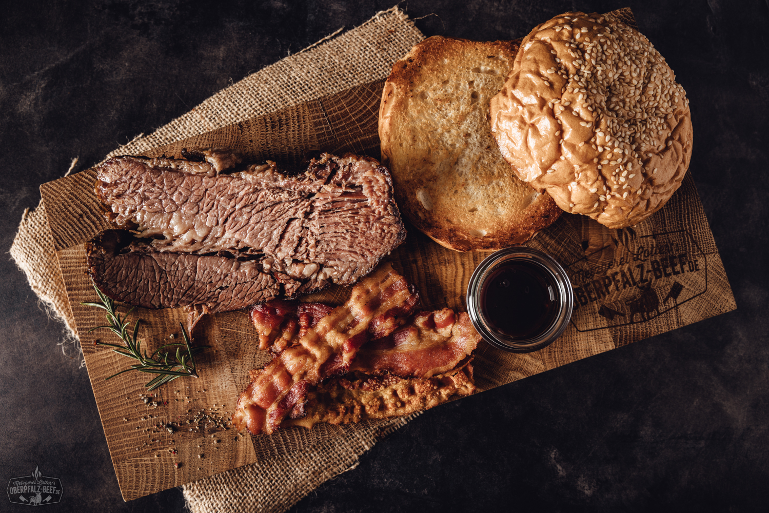 Sous-vide Beef Brisket Box vom Oberpfalz-Rind – zartes Rinderbrustfleisch vorgegart Zart gegarte Beef Brisket Scheiben vom Oberpfalz-Rind, angerichtet auf einem dunklen Holzbrett mit Kräutergarnitur; im Hintergrund Verpackung der Sous-vide vorgegarten Beef Brisket Box – hochwertiges Rindfleisch-Produkt für BBQ und Feinschmecker.