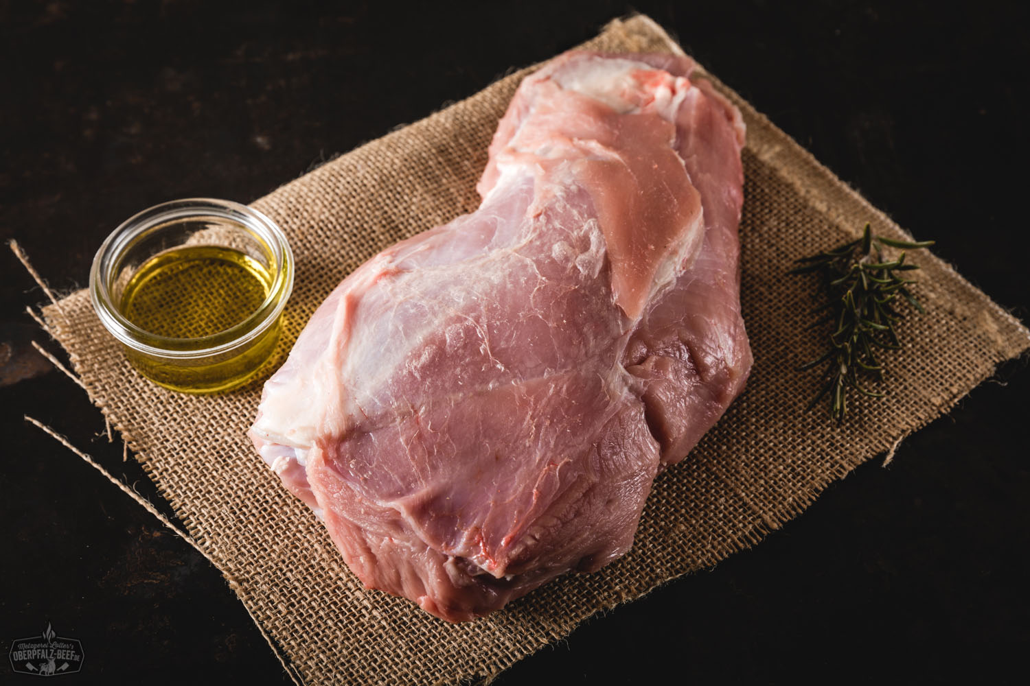 Rohes Halsstück vom Oberpfälzer Milchkalb auf dunkler Unterlage, umgeben von saisonalem Gemüse wie Karotten, Lauch und Zwiebeln, dekorativ angerichtet für Fleischliebhaber und Feinschmecker.