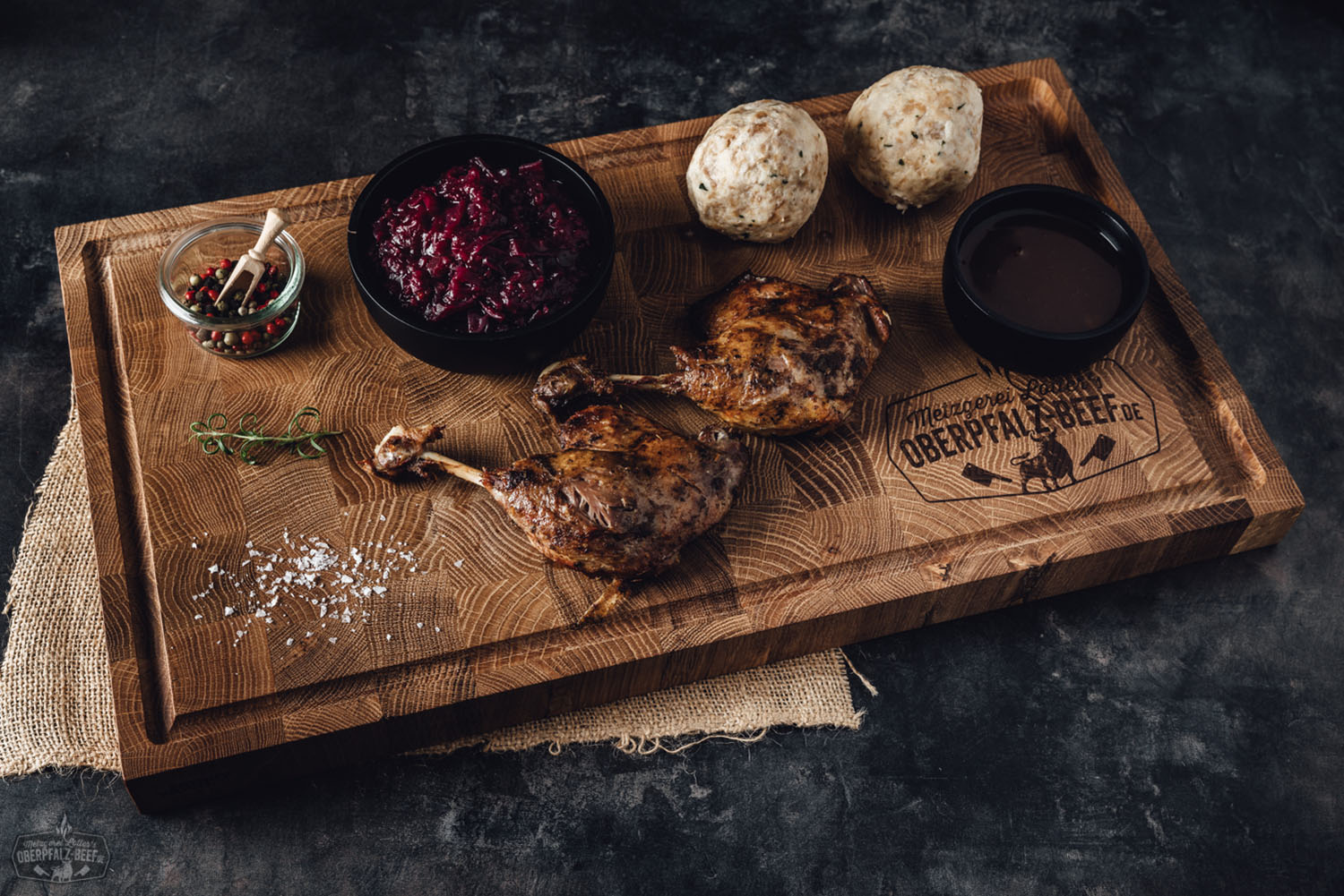 Zart gebratene Entenkeulen mit knuspriger Haut auf Holzbrett angerichtet, begleitet von frischen Orangenscheiben, Kräutern und einer dunklen Bratensoße – traditionelle bayerische Entenspezialität aus der Oberpfalz.