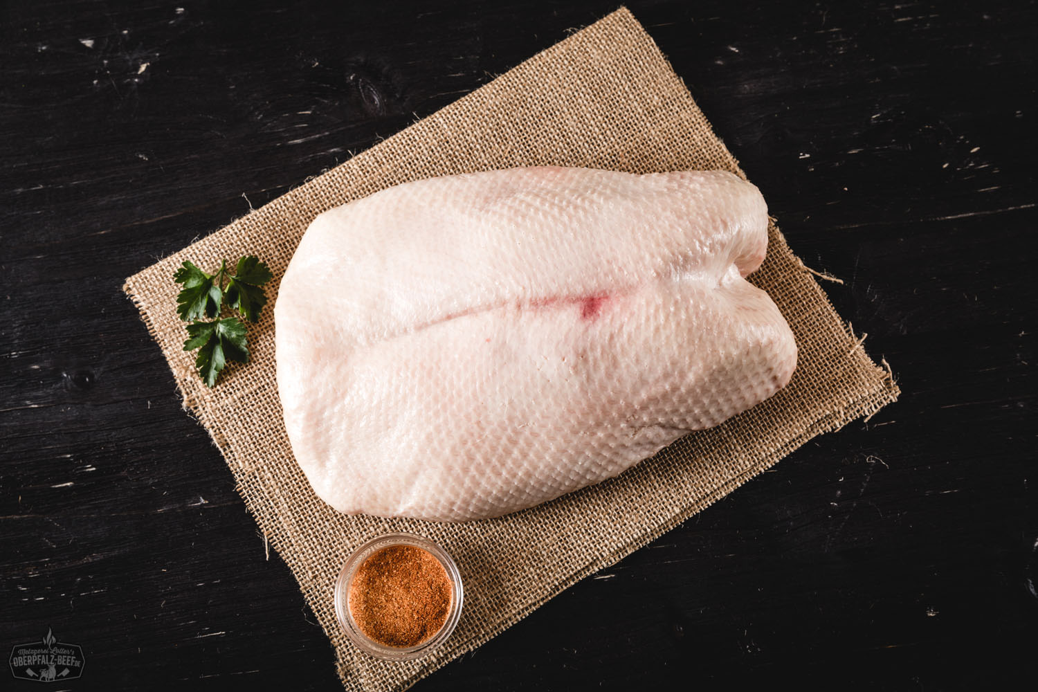 Rohes Brustfilet einer Oberpfälzer Bauerngans auf dunklem Naturstein angerichtet, begleitet von frischen Kräutern, Knoblauch und grobem Meersalz – hochwertige regionale Geflügelspezialität für bewusstes Kochen.