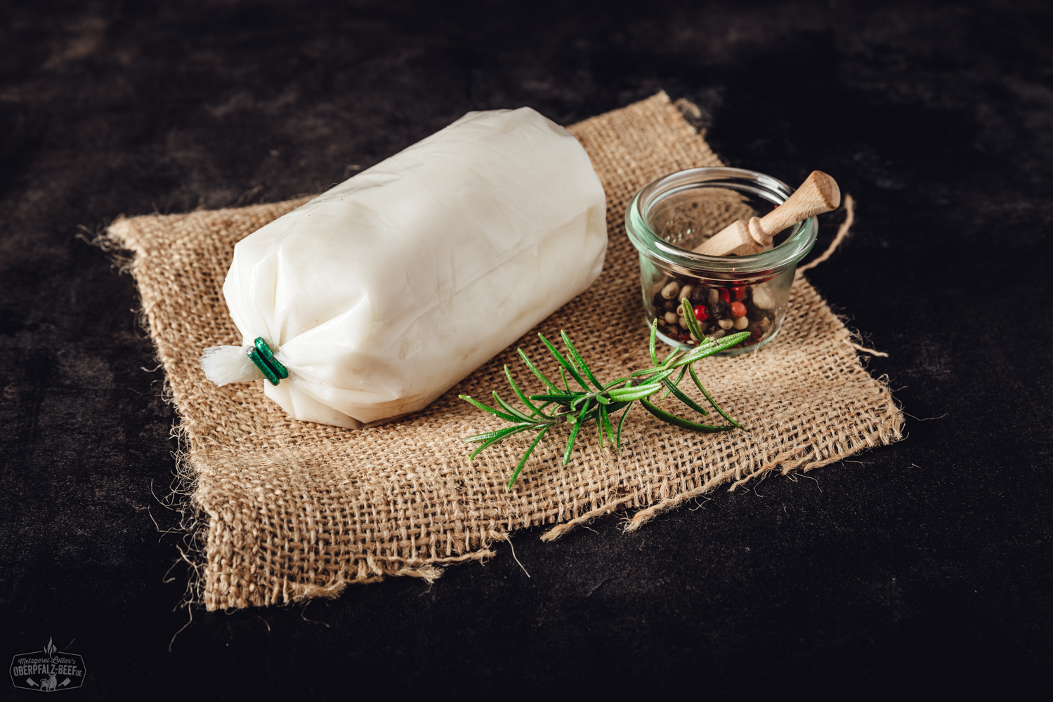 Ausgelassenes Schweinefett in Glas – naturbelassenes Schmalz aus der Oberpfalz Rohe Lammhüfte vom Juradistl-Lamm auf dunkler Schieferplatte, umgeben von Rosmarinzweigen, buntem Pfeffer, grobem Salz und Knoblauchzehen – hochwertige Fleischspezialität für bewusste Genießer.