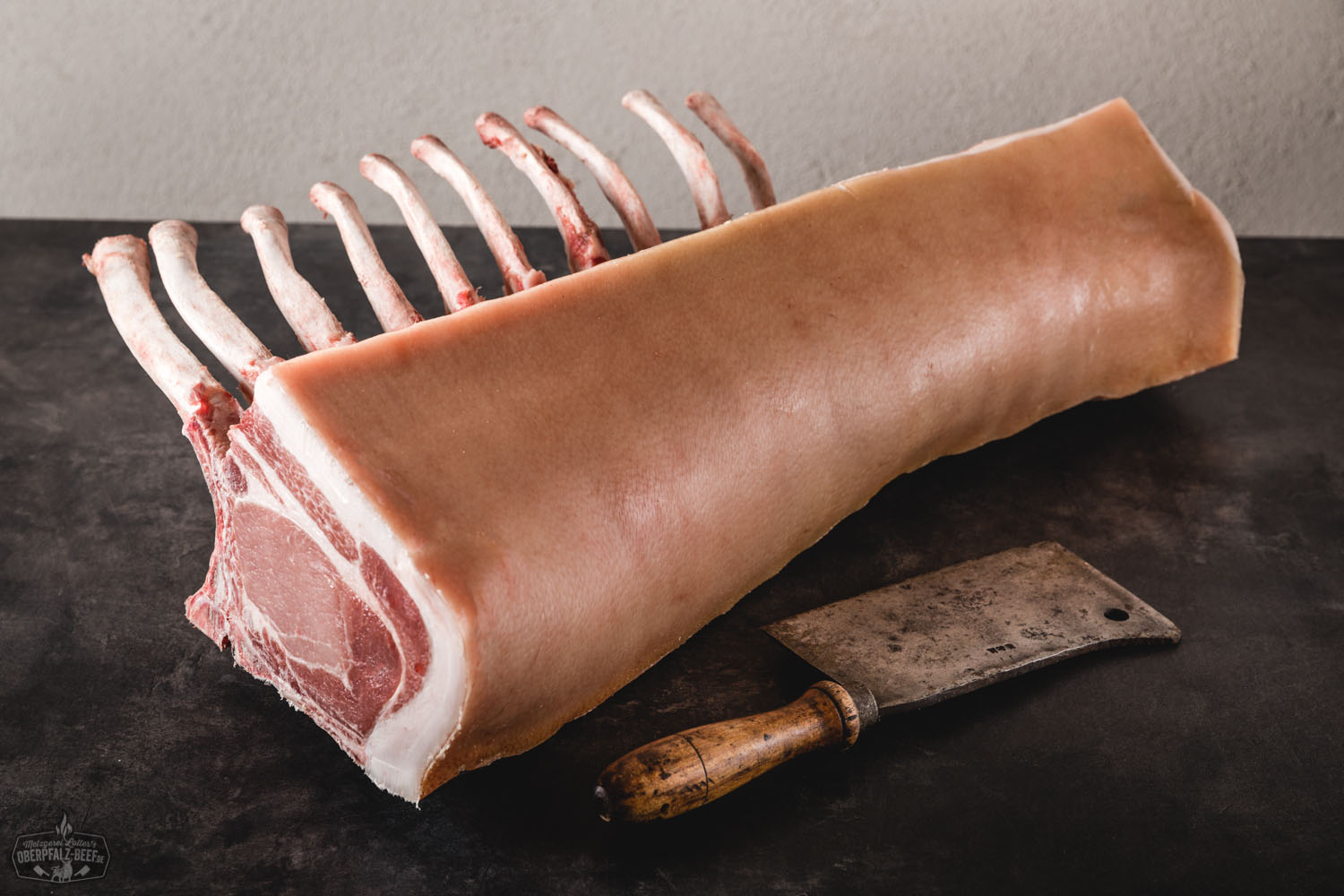 Tomahawk-Kotelett vom Oberpfälzer Landschwein – Frisch & Regional Frisches Tomahawk-Kotelett vom Oberpfälzer Landschwein roh auf dunklem Holzuntergrund, mit deutlich sichtbarem langen Rippenknochen, marmorierter Fleischstruktur und kräftiger roter Farbe; ideales Premiumstück für Grill oder Pfanne.