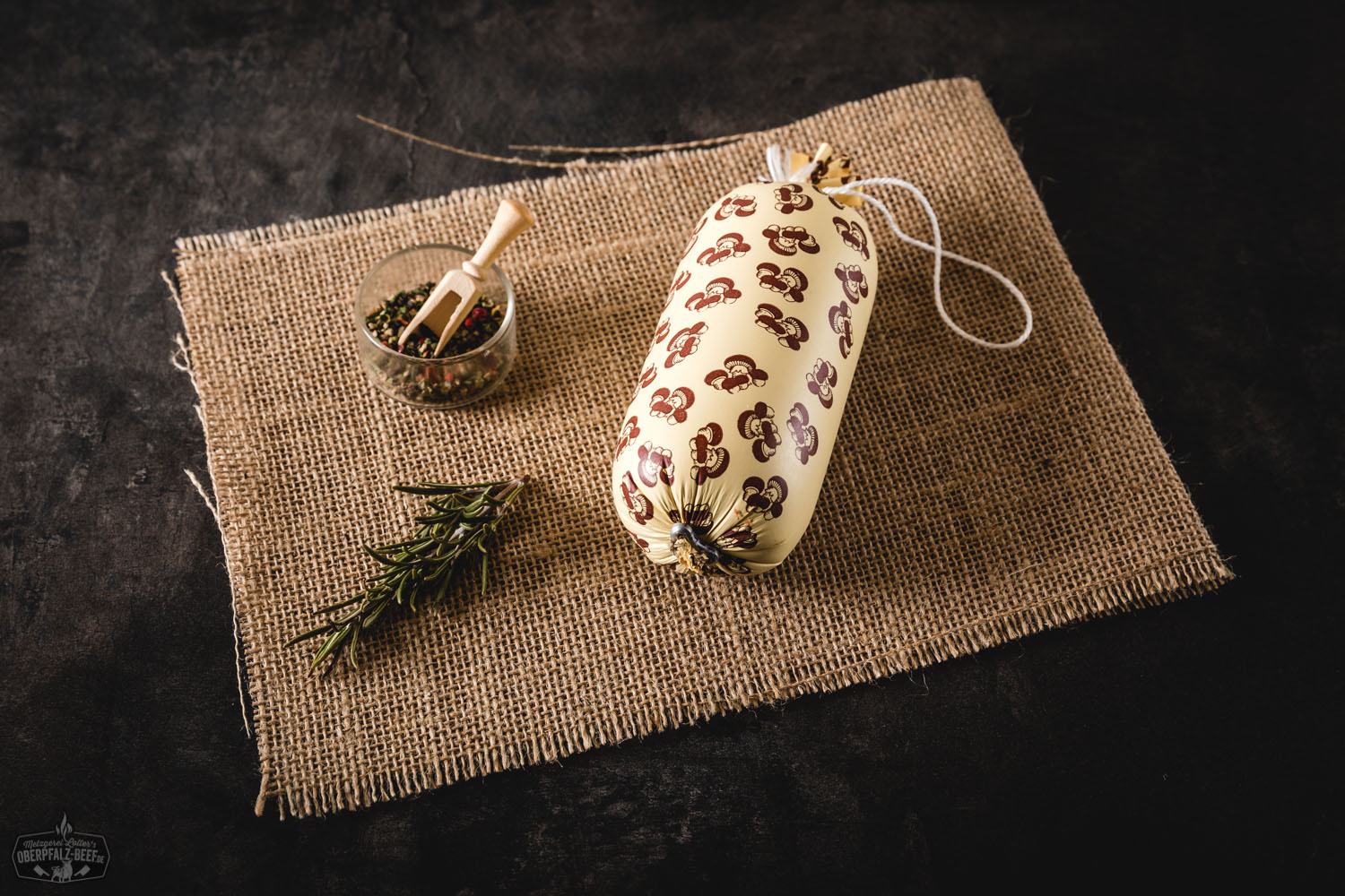 Geschnittene Champignonwurst auf Holzbrett, umgeben von frischen Champignons und Schnittlauch, rustikale Präsentation der feinen Wurst mit sichtbaren Pilzstücken – ideal für Brotzeit oder Vesper.