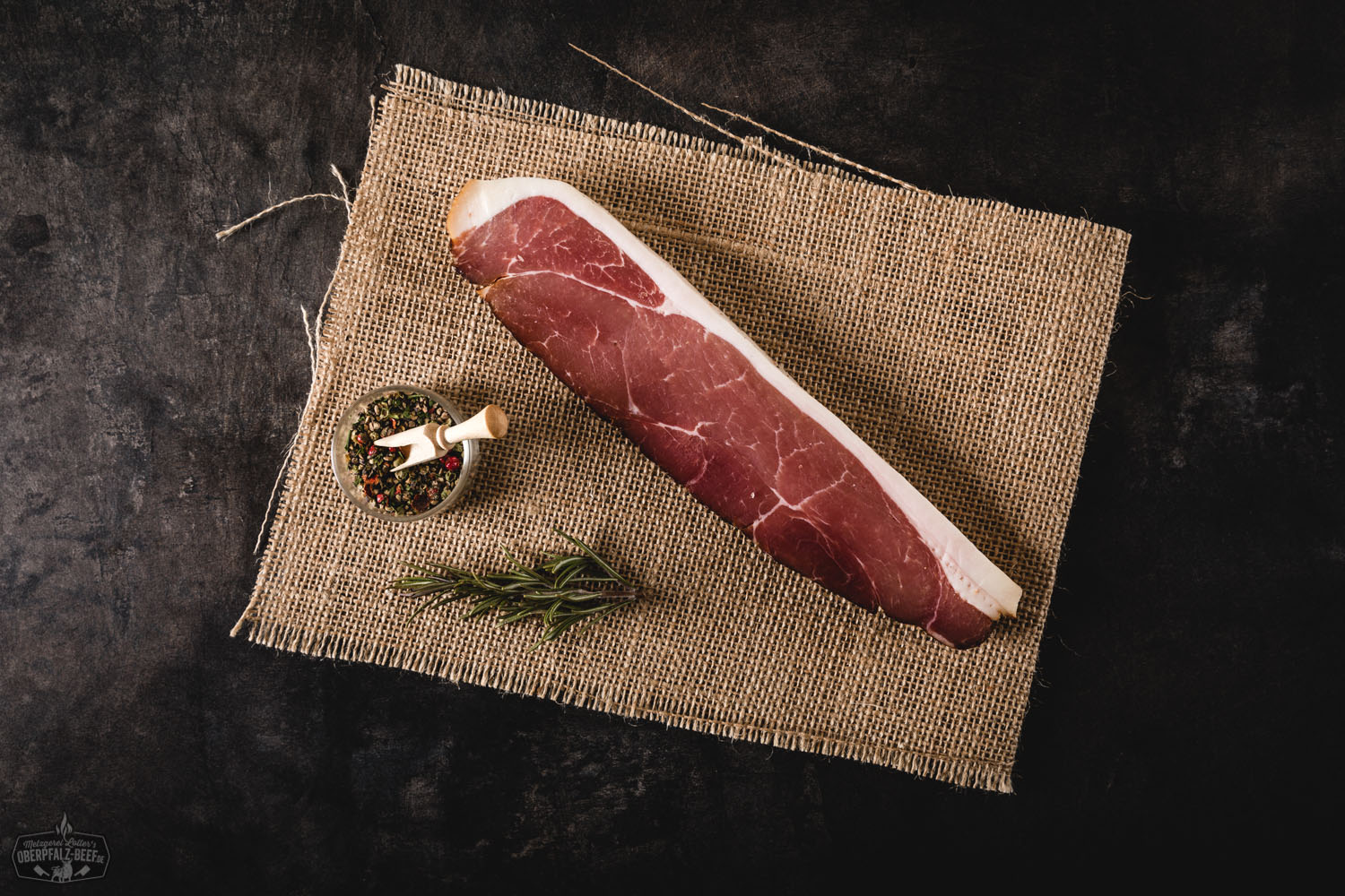 Traditionelle Brotzeitscheibe mit Oberpfälzer Bauern-Geselchtem aus dem Schlegel auf Holzbrett, serviert mit Gewürzgurke, frischem Bauernbrot und rustikaler Dekoration – typisch bayerische Spezialität.