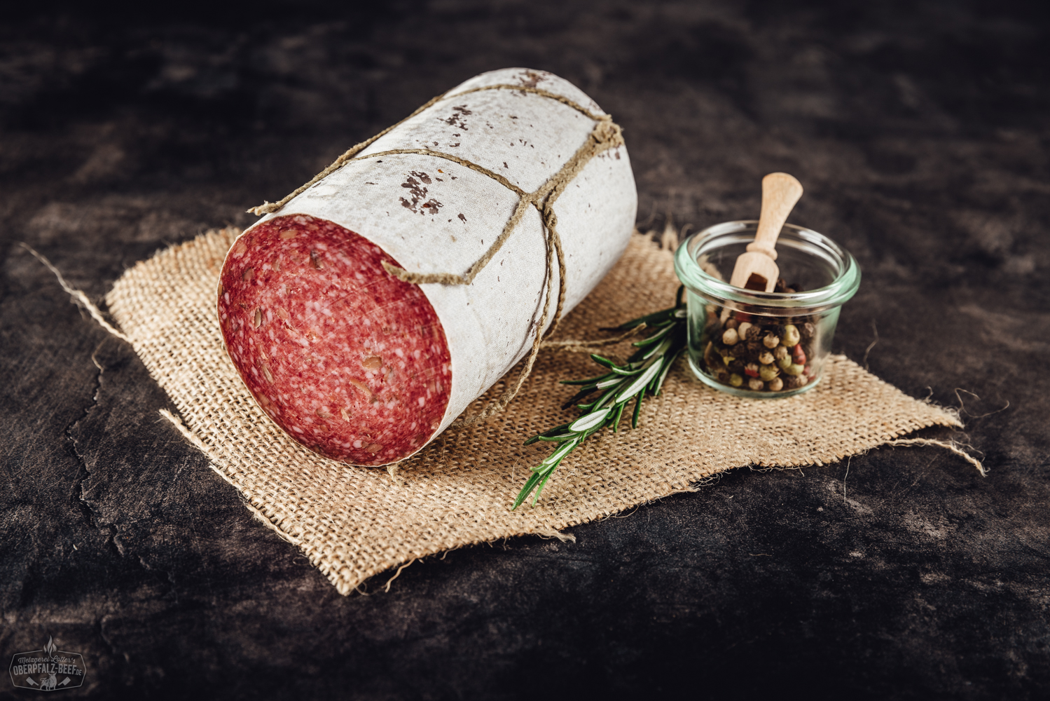 Geschnittene Kürbiskernsalami auf Holzbrett – Delikatesswurst aus der Oberpfalz Geschnittene Trüffelsalami auf einem dunklen Schieferbrett, dekorativ angerichtet mit Kräutern und einem Trüffelpilz; hochwertige Delikatesswurst mit sichtbaren Trüffelstücken – perfekte Auswahl für Feinschmecker und Trüffel-Liebhaber.