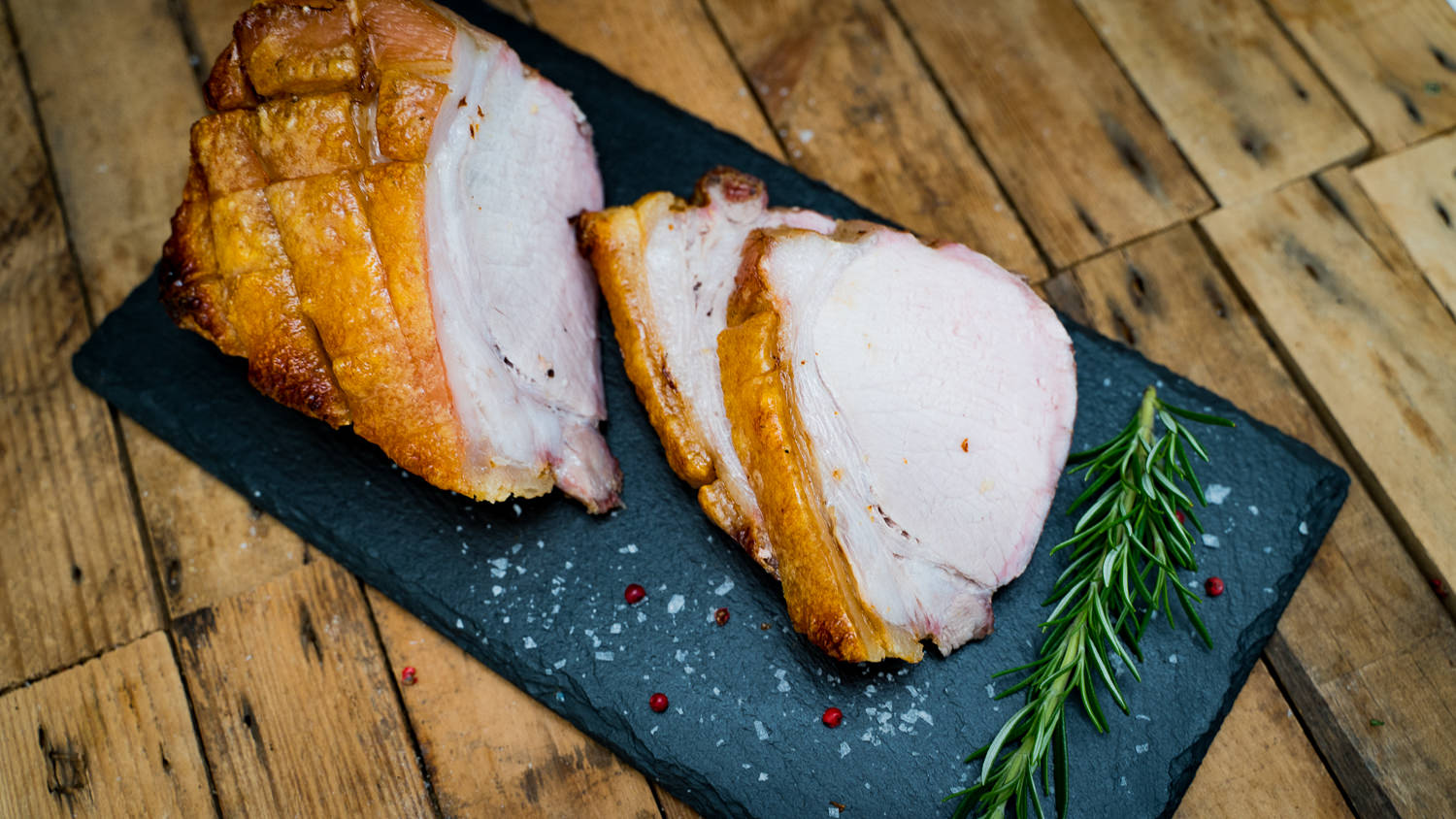 Dry Aged Kotelett mit Schwarte vom Oberpfälzer Landschwein – Halbes Stück Premiumqualität Halbes Dry-Aged Kotelett vom Oberpfälzer Landschwein mit Schwarte, roh und sauber zugeschnitten, auf dunkler Steinplatte mit Salz, Rosmarin und Knoblauch arrangiert – hochwertiges Fleisch in Premiumqualität für Steak- und Grillliebhaber.