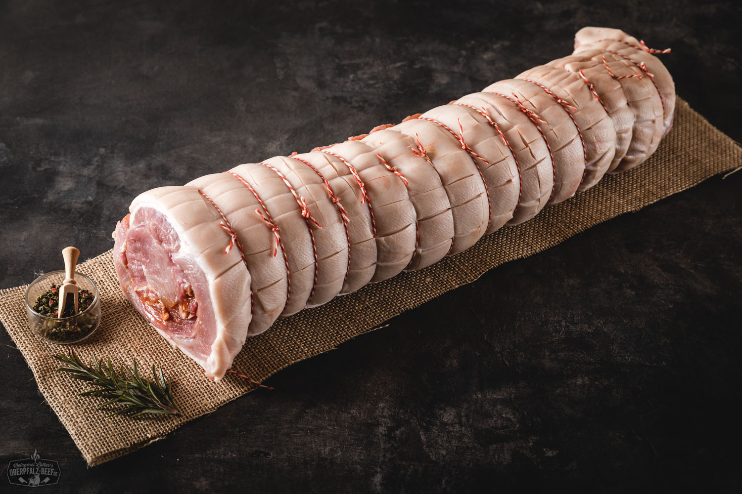 Spanferkelrollbraten vom Oberpfälzer Landschwein, goldbraun knusprig gebraten, aufgeschnitten und saftig auf einem Holzbrett serviert, mit frischen Kräutern und knuspriger Kruste – traditionelles bayerisches Braten-Gericht.