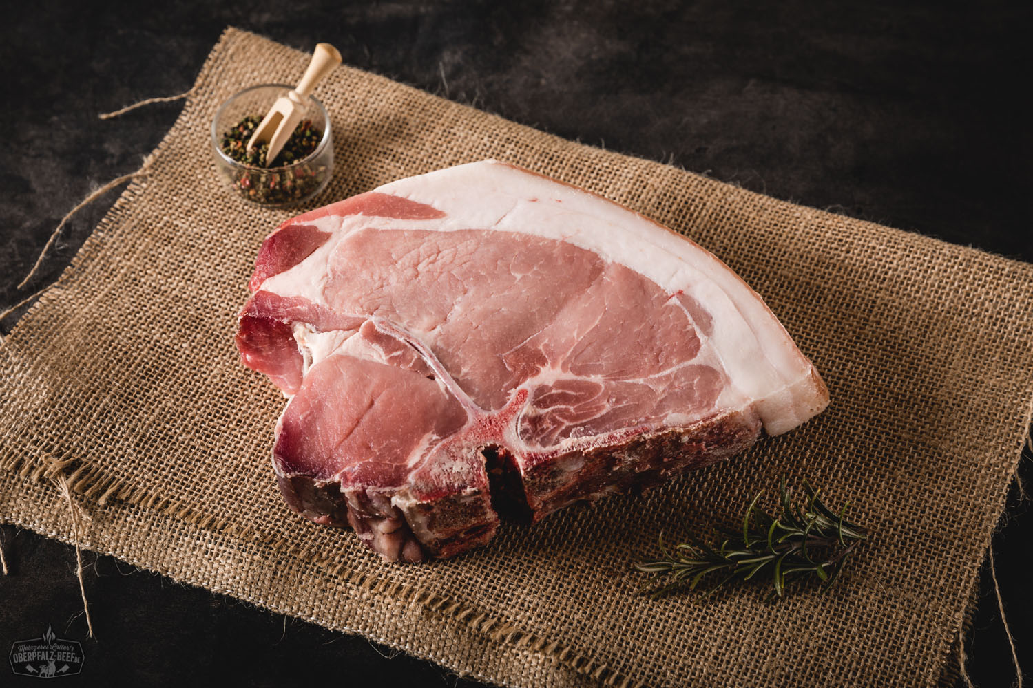 T-Bone-Steak vom Oberpfälzer Landschwein, dry aged, roh auf dunklem Holzuntergrund angerichtet – gut marmoriertes Fleisch mit deutlichem Knochenanteil, ideal zum Grillen oder Braten, hochwertige Fleischspezialität aus regionaler Aufzucht.