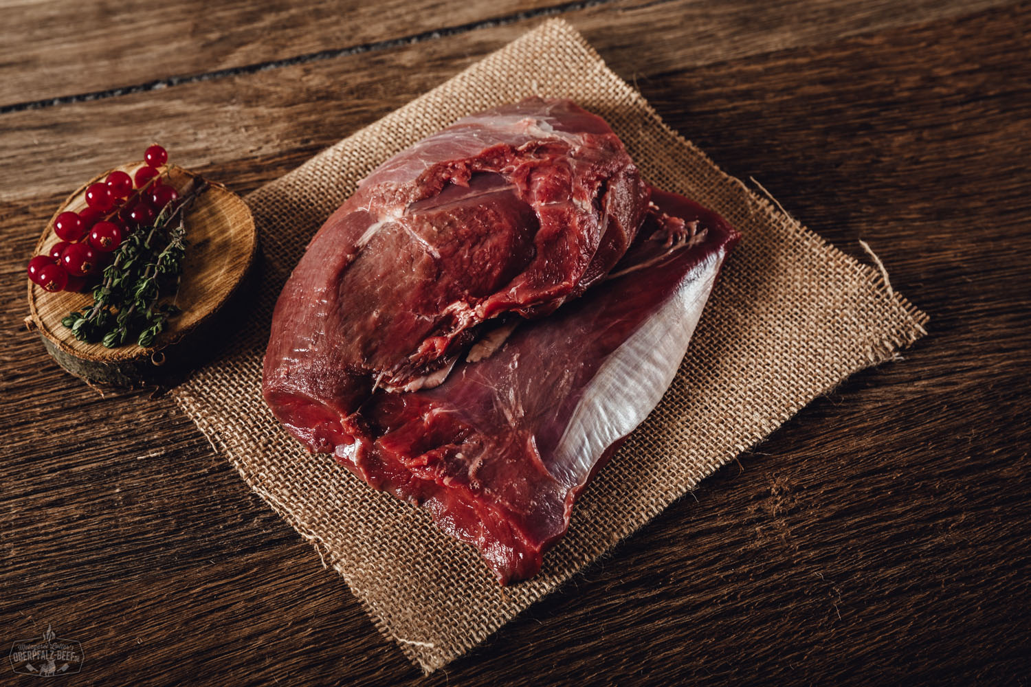 Schulter ohne Knochen vom Oberpfälzer Reh – Wildfleisch in Premiumqualität Rohes, entbeintes Rehschulterstück vom Oberpfälzer Reh auf dunkler Schieferplatte angerichtet, umgeben von frischen Kräutern, Wacholderbeeren und Gewürzen – hochwertige Wildfleisch-Delikatesse aus regionaler Jagd.