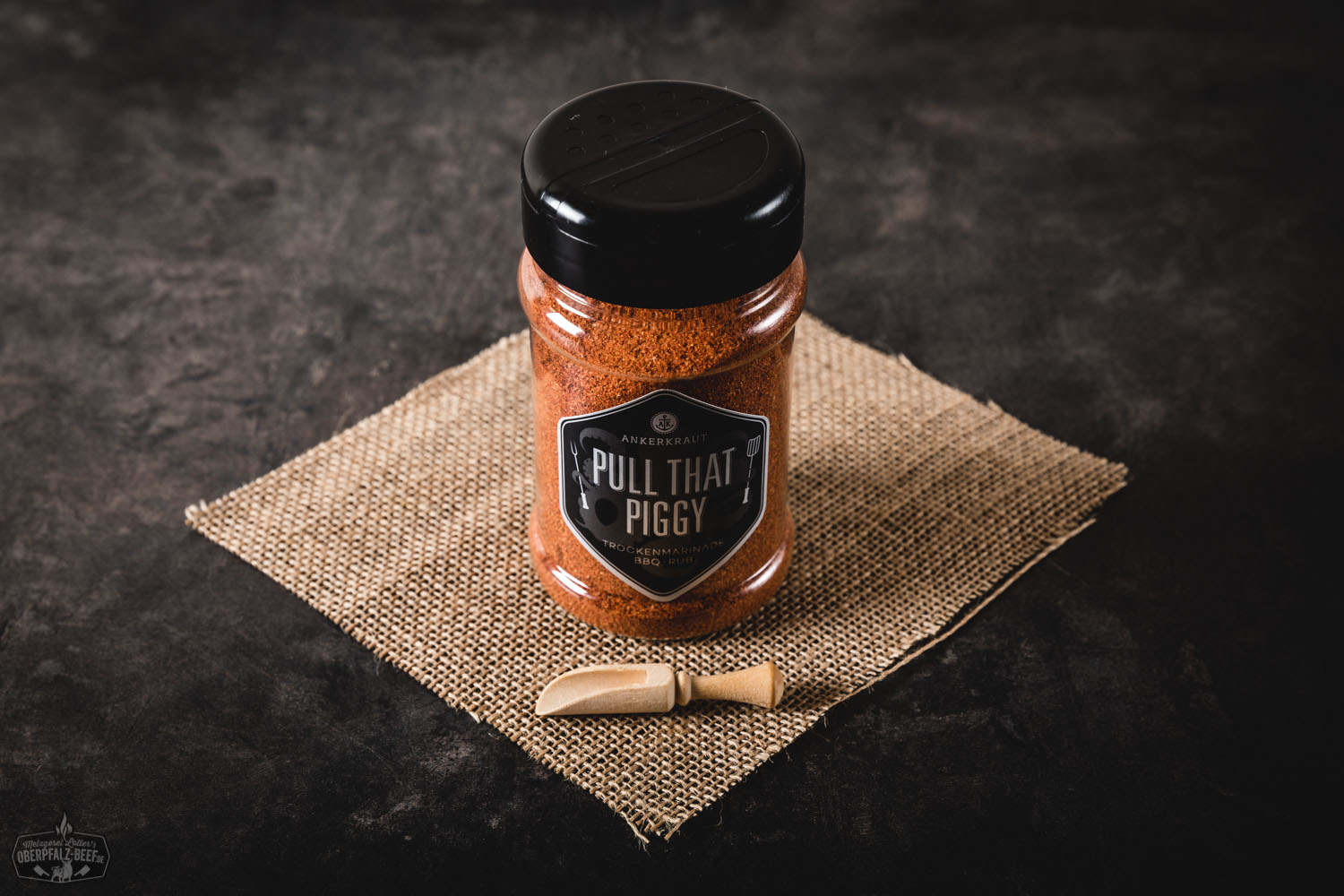 Ankerkraut BBQ Rub „Pull that Piggy“ im Streuer – Würzmischung für Pulled Pork Gewürzstreuer „Pull That Piggy“ von Ankerkraut mit Schweinefleisch-Gewürzmischung auf dunklem Holztisch, daneben lose Gewürze und BBQ-Zubehör – ideal für Pulled Pork und Grillgerichte.