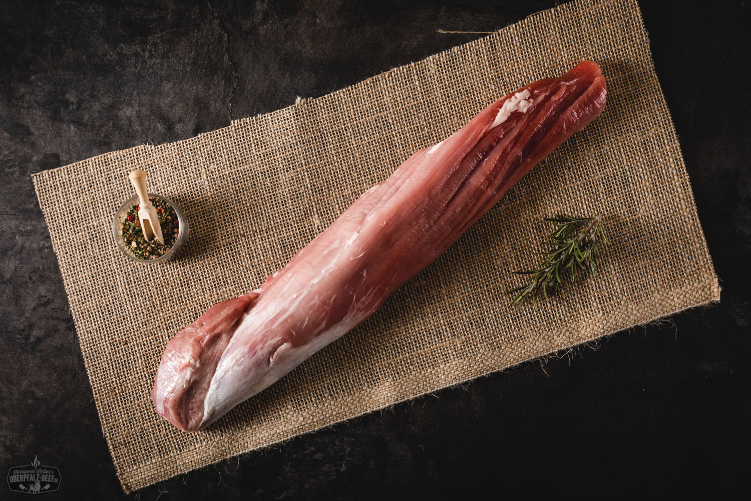 Rohes Filet oder Lende vom Oberpfälzer Landschwein, frisch zugeschnitten auf hellem Holzbrett, mit Rosmarinzweig und grobem Meersalz dekoriert – hochwertige Schweinefleischdelikatesse aus regionaler Zucht.