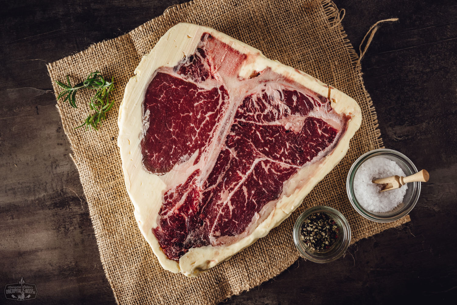 Porterhouse Steak Butter Aged vom Oberpfalz Rind – Premium Beef Genuss aus Bayern Porterhouse-Steak vom Oberpfalz-Rind, medium gegrillt, mit goldbrauner Fleischkruste, trocken gereift (Butter Aged), auf Holzbrett serviert, daneben frische Rosmarinzweige und Meersalz – hochwertiges Dry-Aged-Steak für Grillgenuss und Fleischliebhaber.